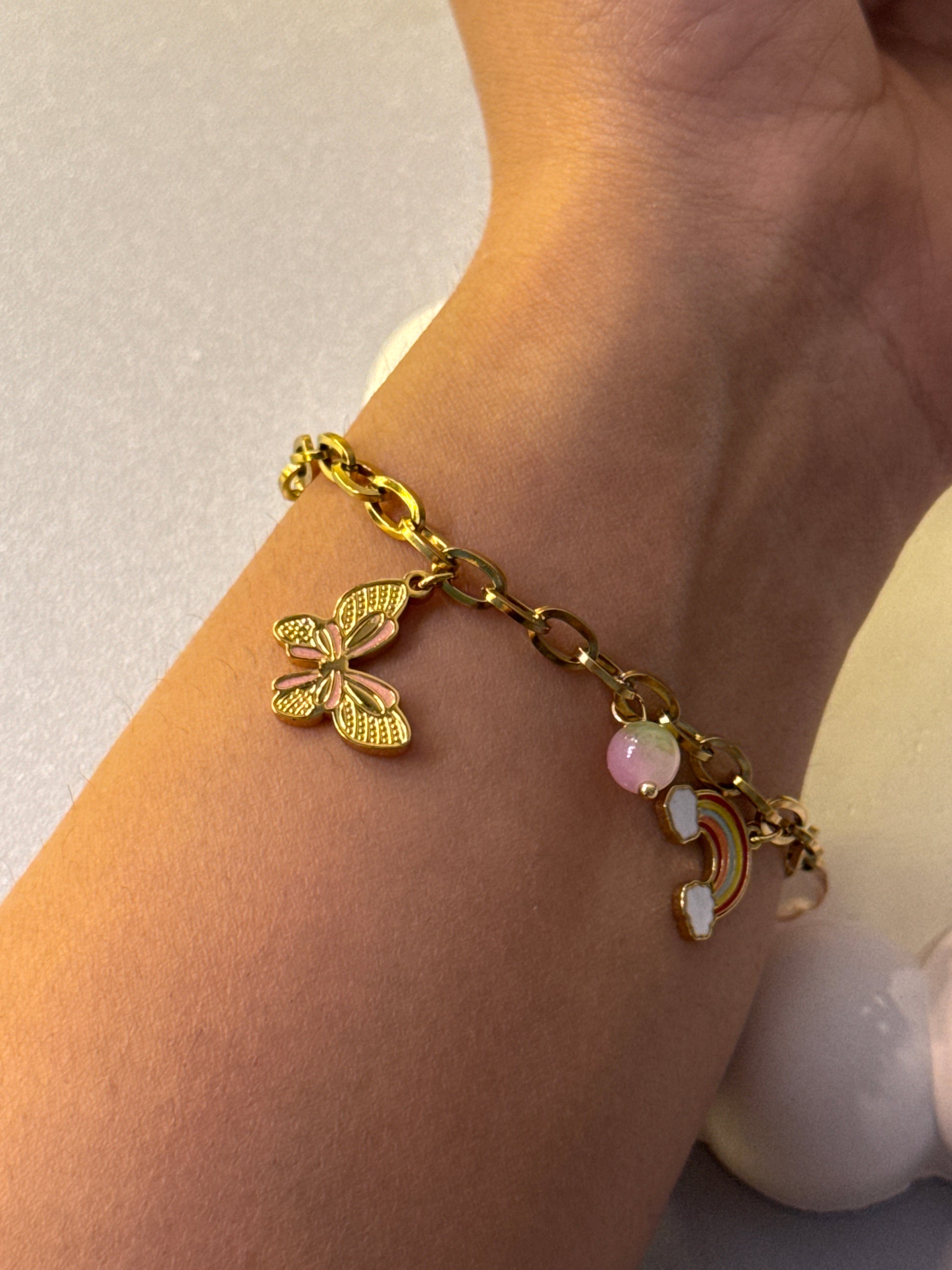 Gold bracelet with butterfly charm on a wrist against a neutral background