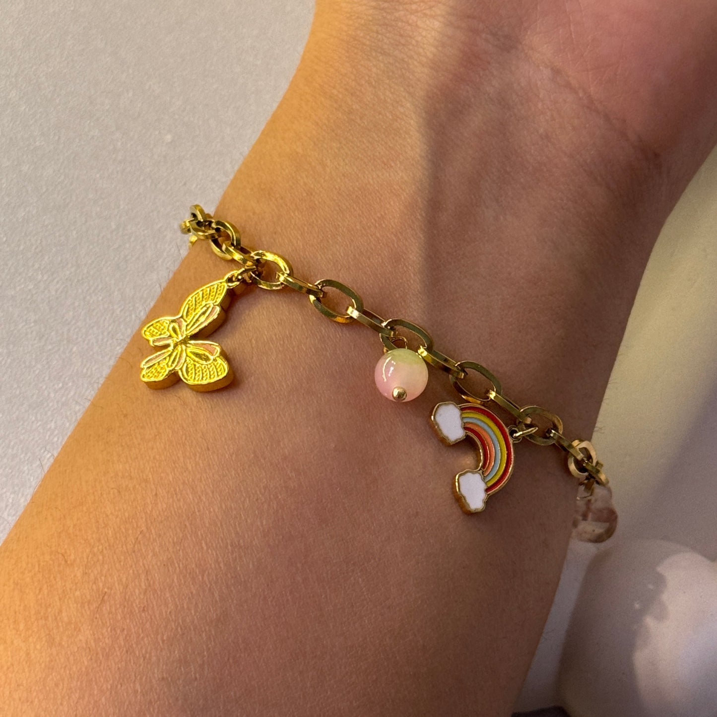 Gold bracelet with butterfly and rainbow charm on wrist
