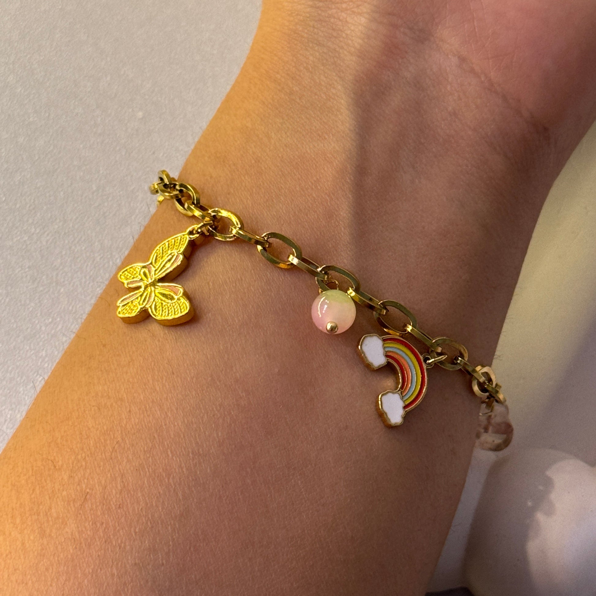 Gold bracelet with butterfly and rainbow charm on wrist