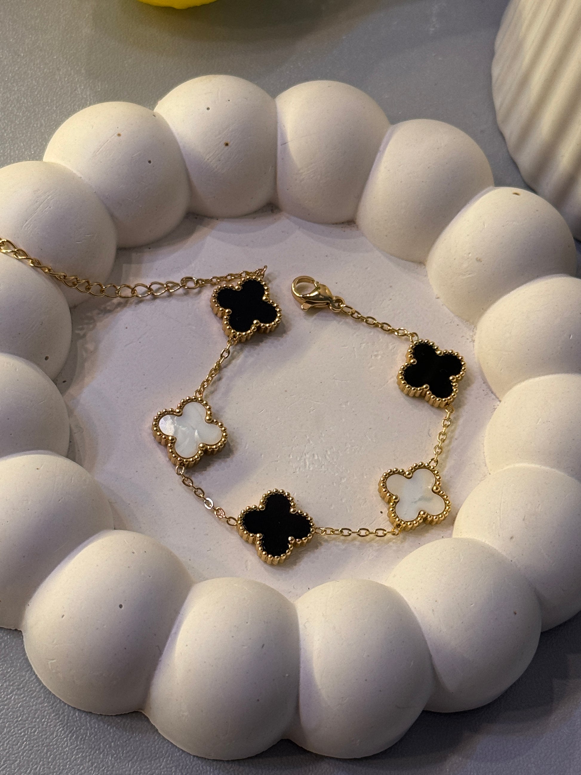 Gold bracelet with black and white clover charms on a white stone surface