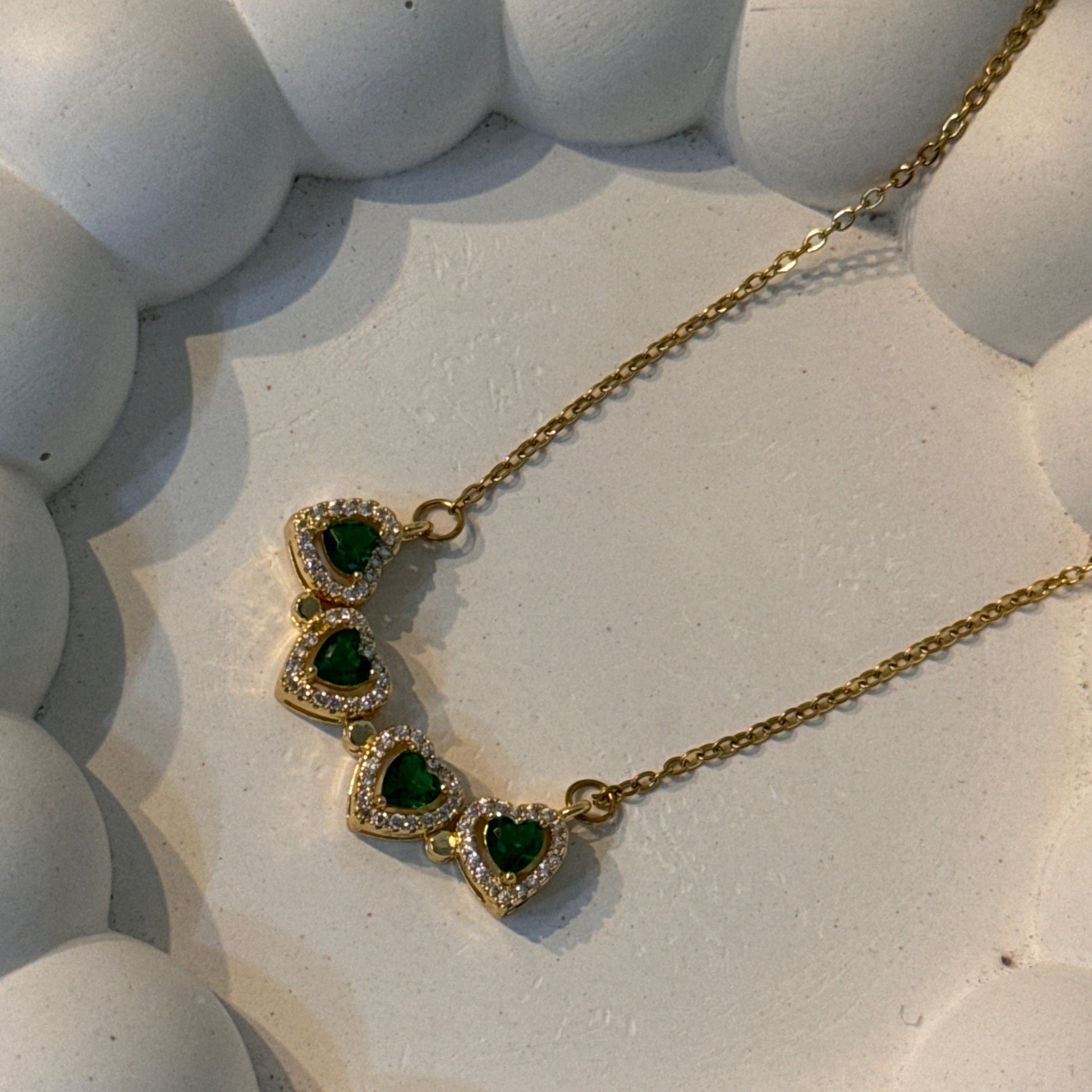 Gold necklace with green gemstones on a textured white surface