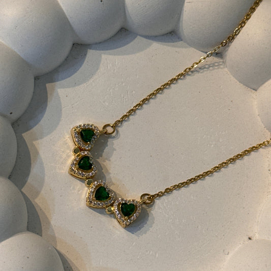 Gold necklace with green gemstones on a textured white surface
