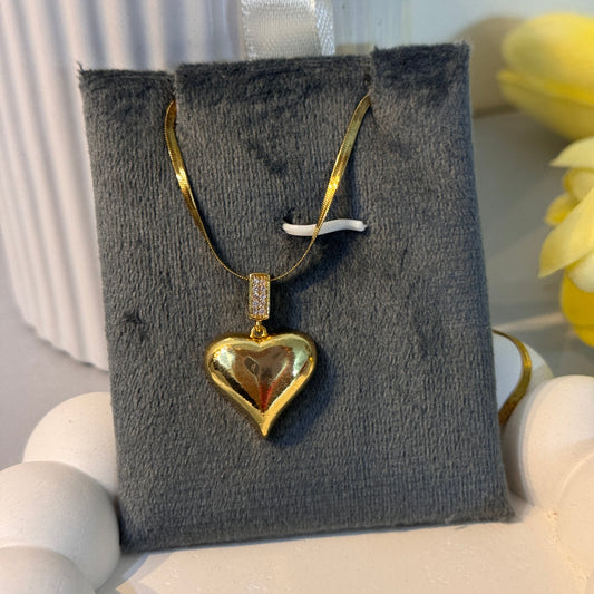 Gold heart-shaped earring on a gray jewelry display card with white flowers in the background.