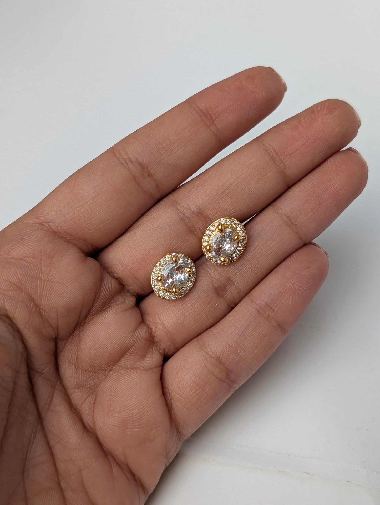 Two diamond stud earrings held in a hand against a white background