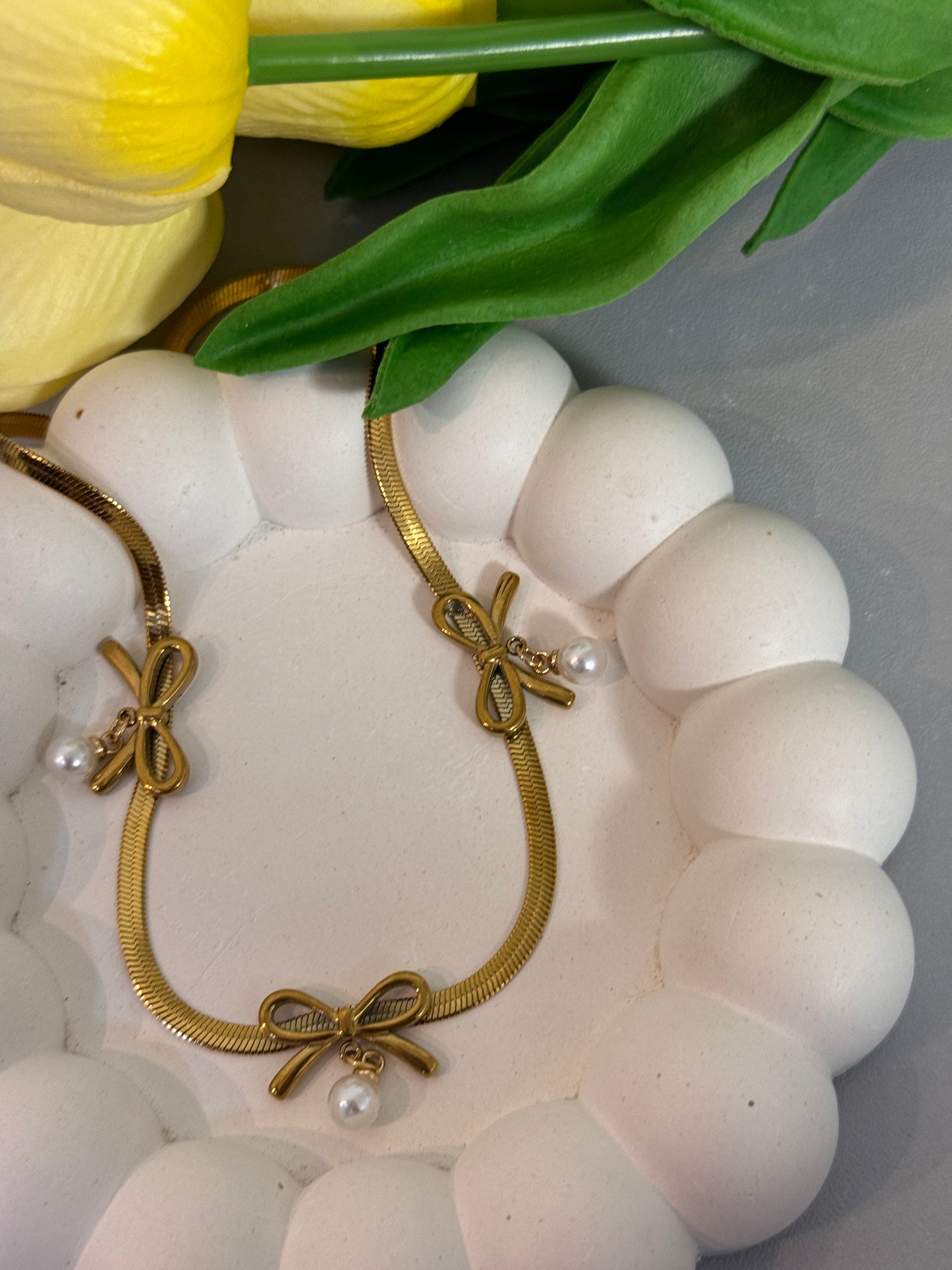 Gold bracelet with bow and pearl accents on a white shell with tulips in the background