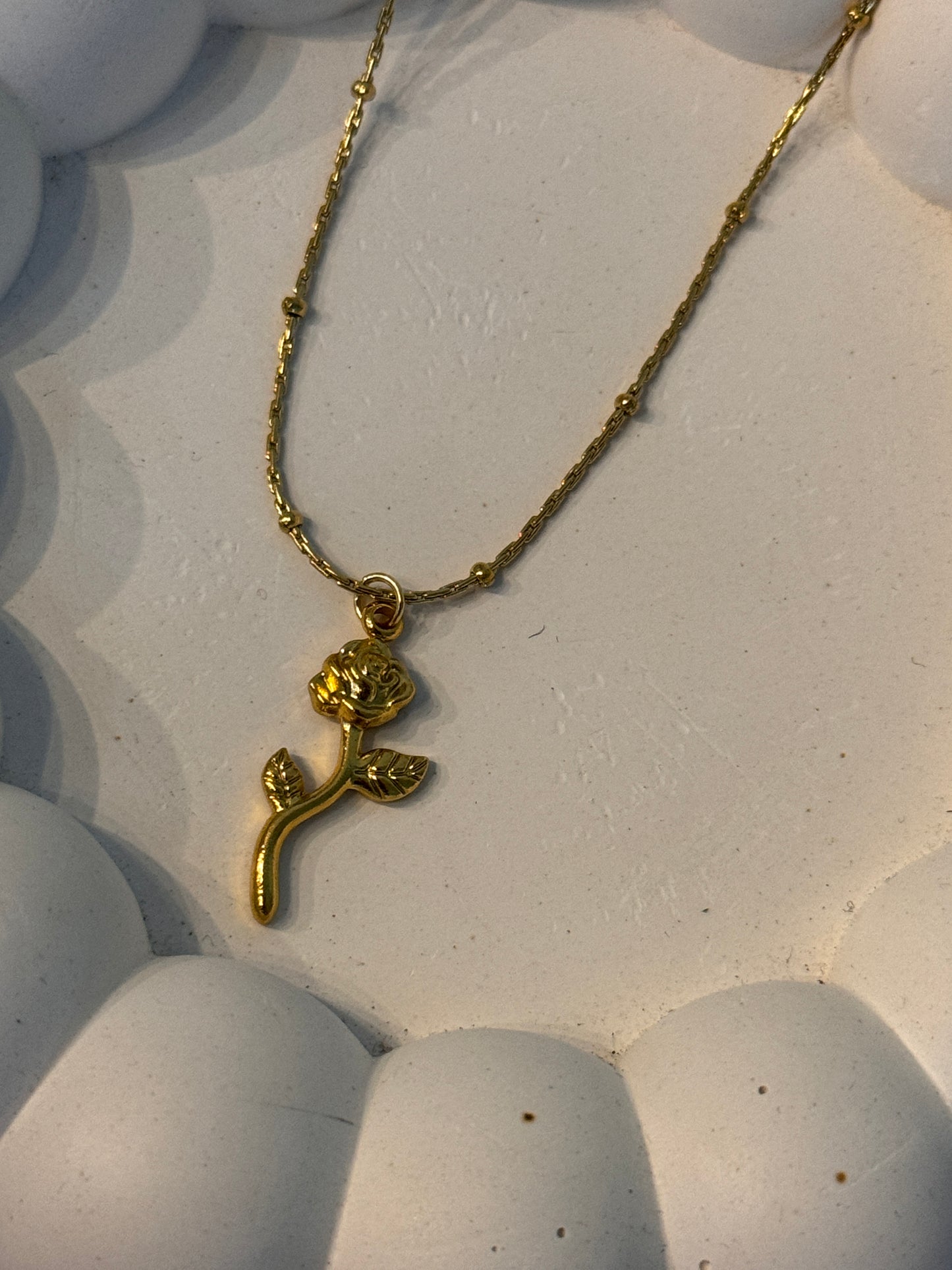 Gold necklace with a floral pendant on a textured white surface