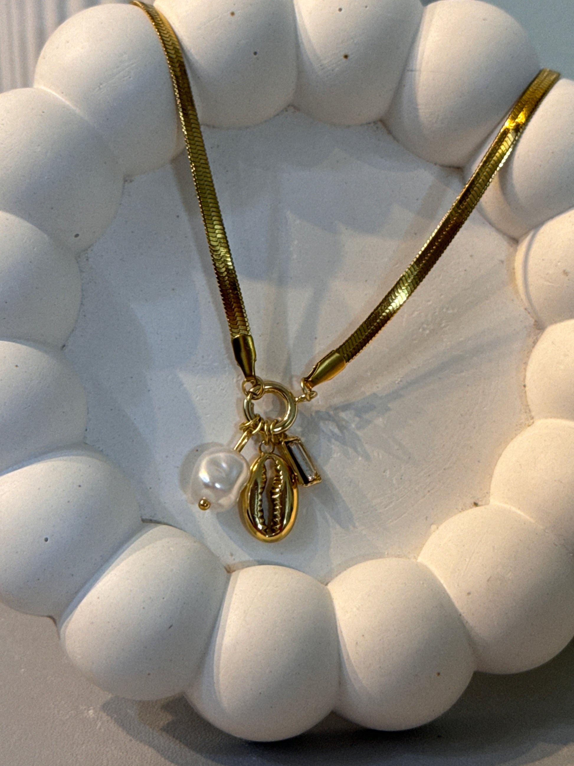 White beaded bracelet with a gold clasp on a textured white surface