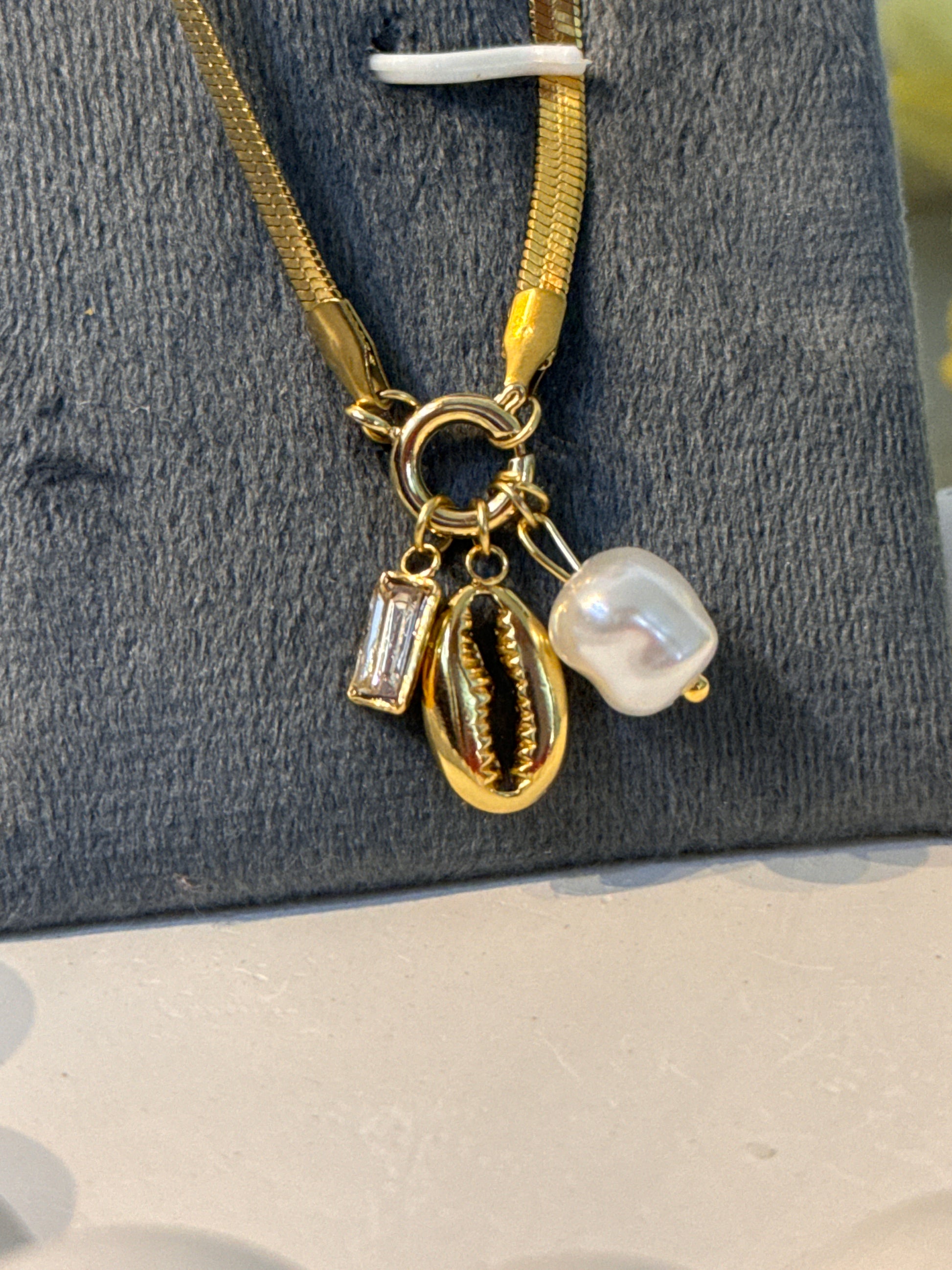 Gold necklace with a pendant featuring a pearl and clear gemstone on a textured surface.