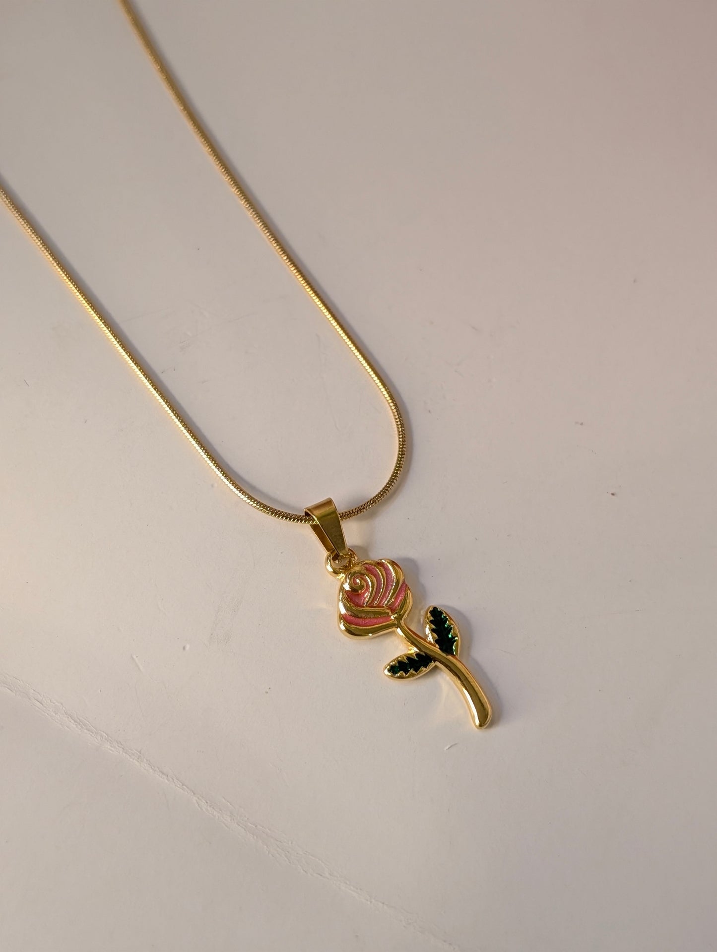 Gold necklace with a rose pendant on a light gray background