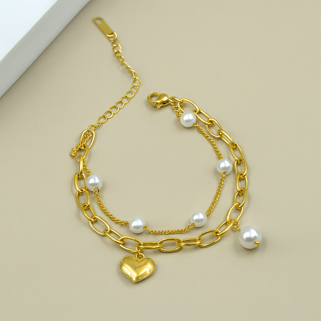 Gold chain bracelet with heart charm and pearls on a beige background