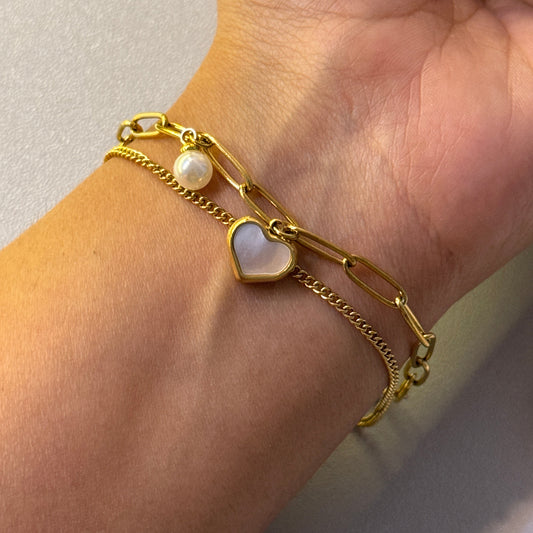 Gold chain bracelet with heart-shaped charms on a wrist against a neutral background