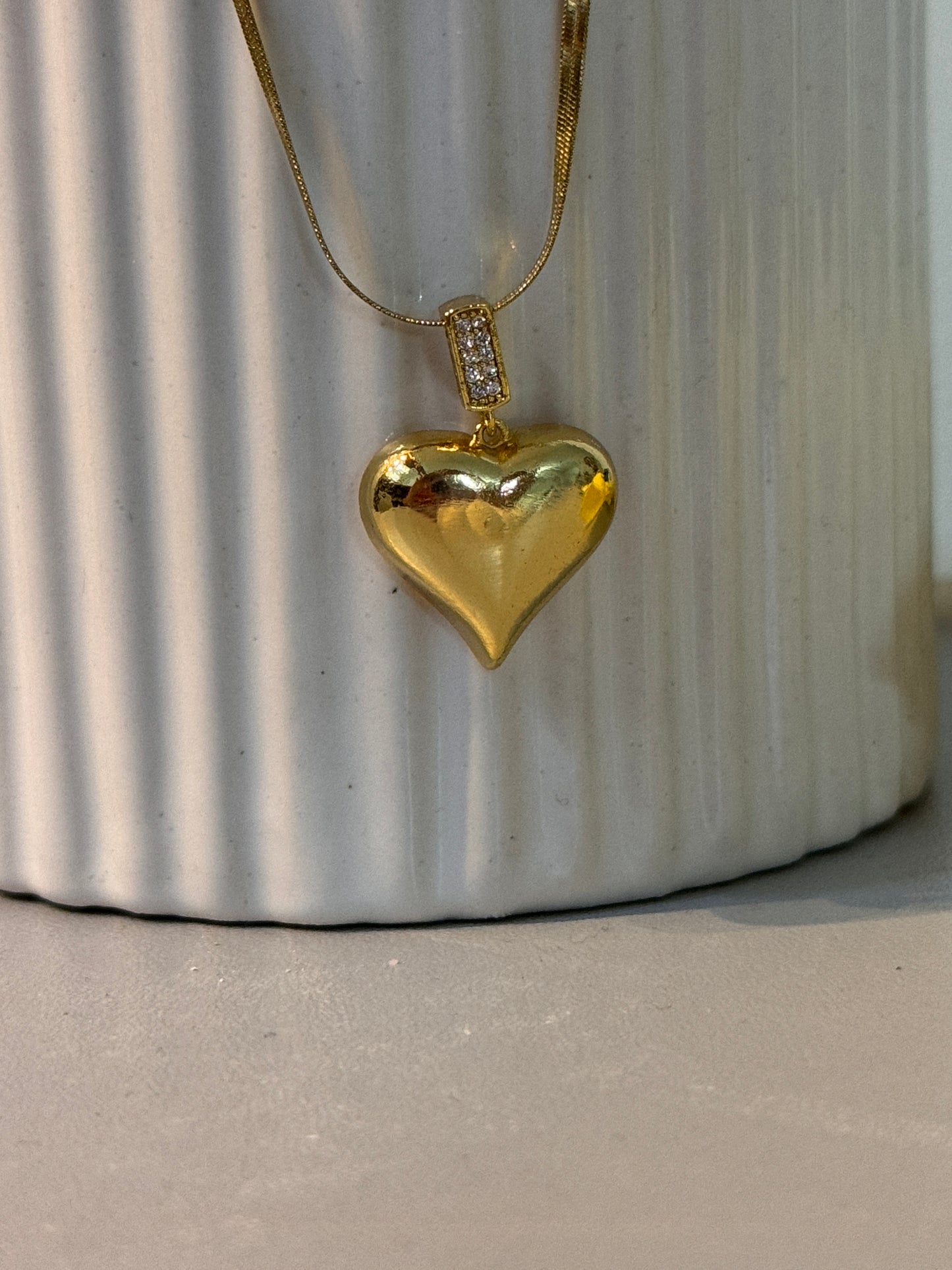 Gold necklace with a heart-shaped pendant on a textured surface