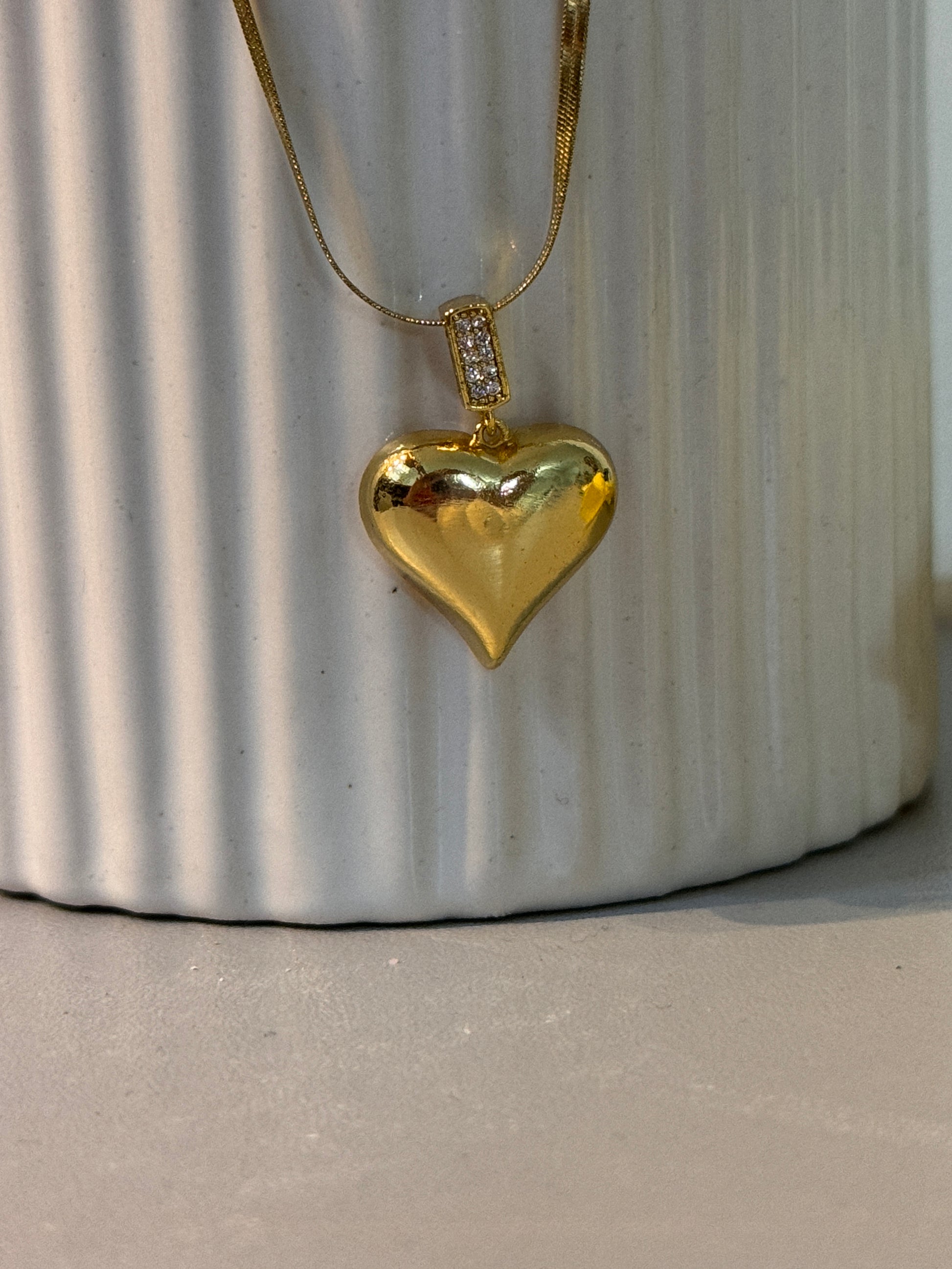 Gold necklace with a heart-shaped pendant on a textured surface