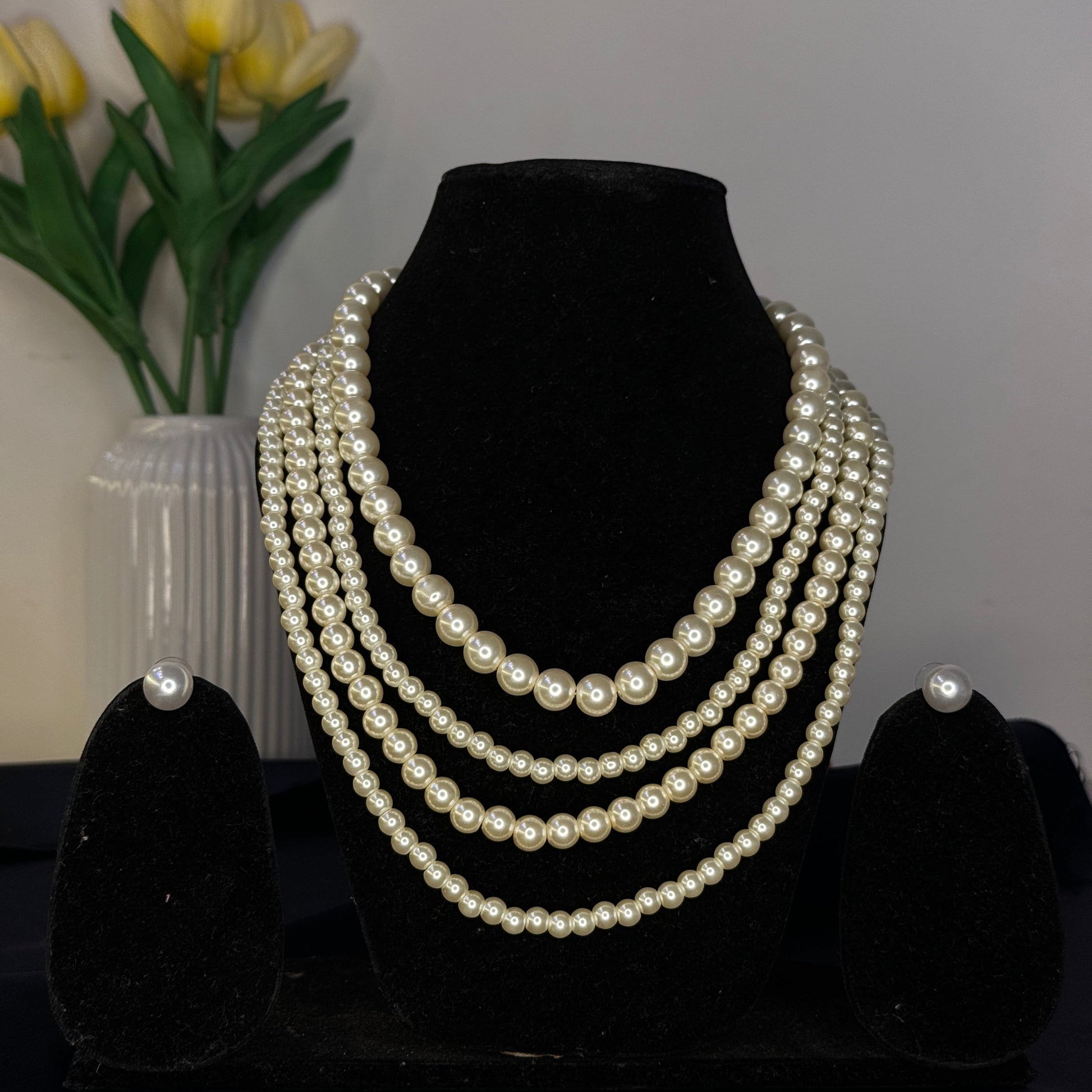 Set of pearl necklaces on a black stand with yellow tulips in the background