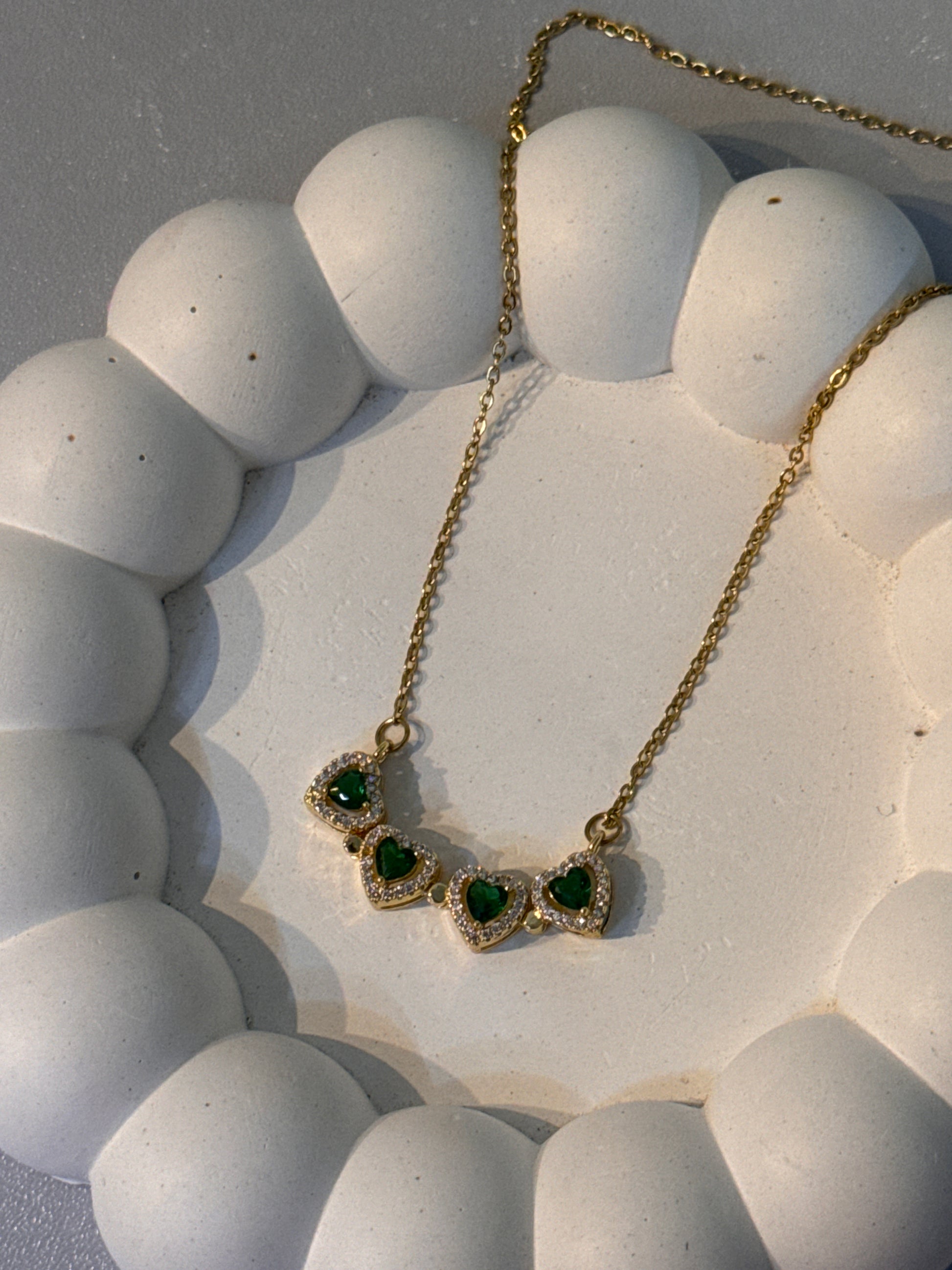 Gold necklace with green gemstones on a textured white surface