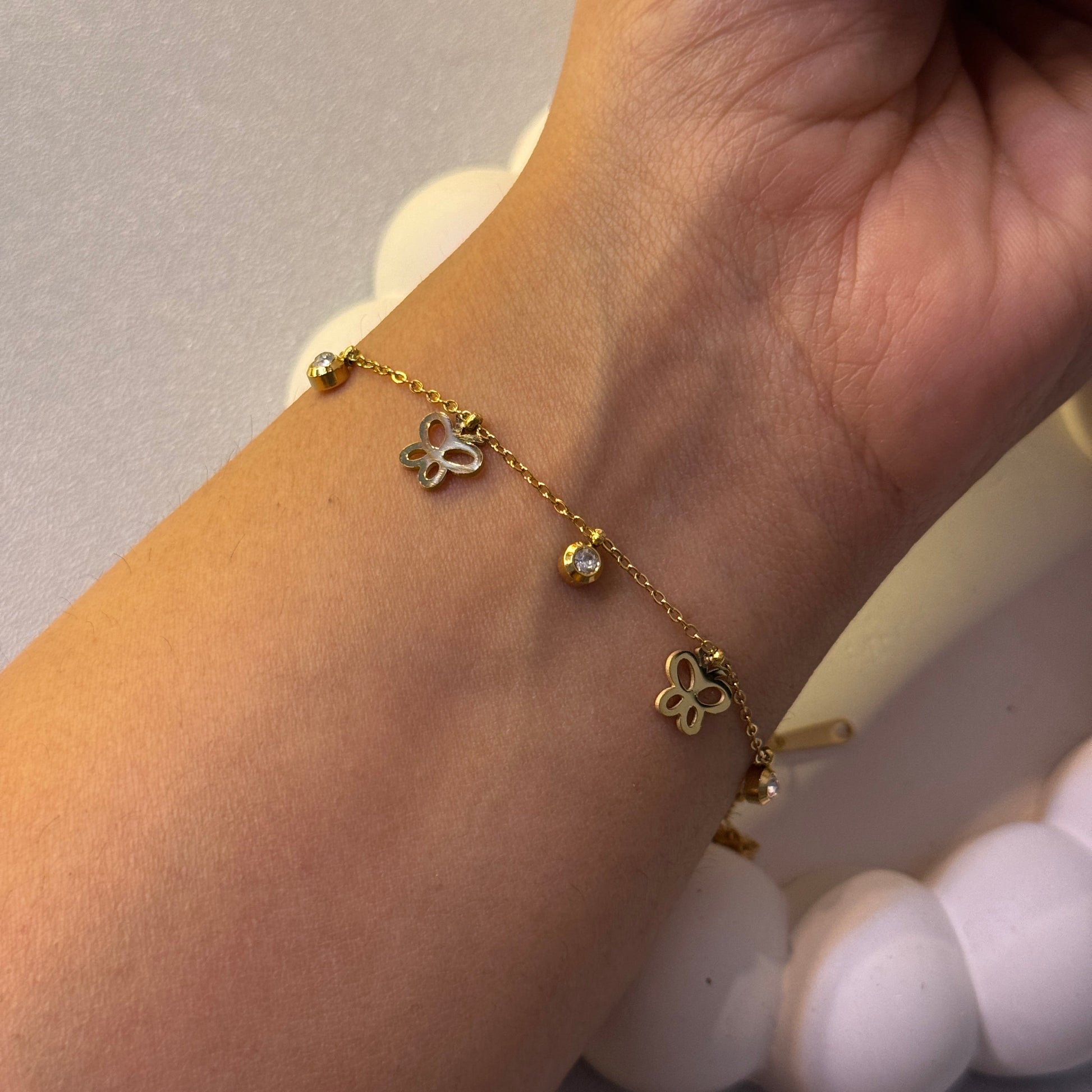 Gold bracelet with butterfly charms on a wrist against a neutral background