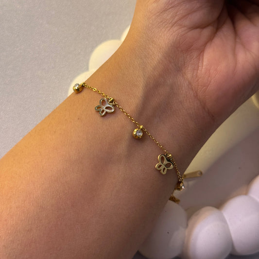 Gold bracelet with butterfly charms on a wrist against a neutral background