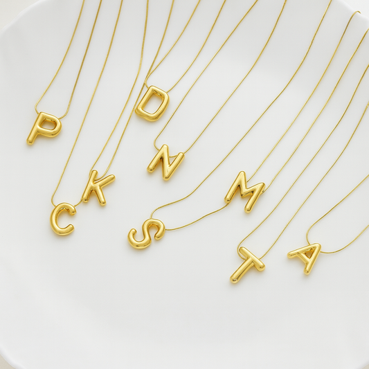 Gold necklaces with letter pendants on a white surface
