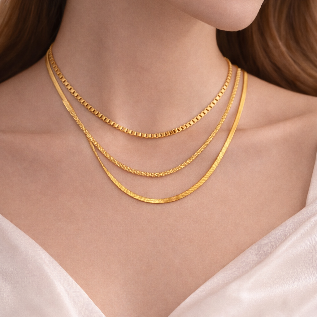Two gold necklaces on a person wearing a white top