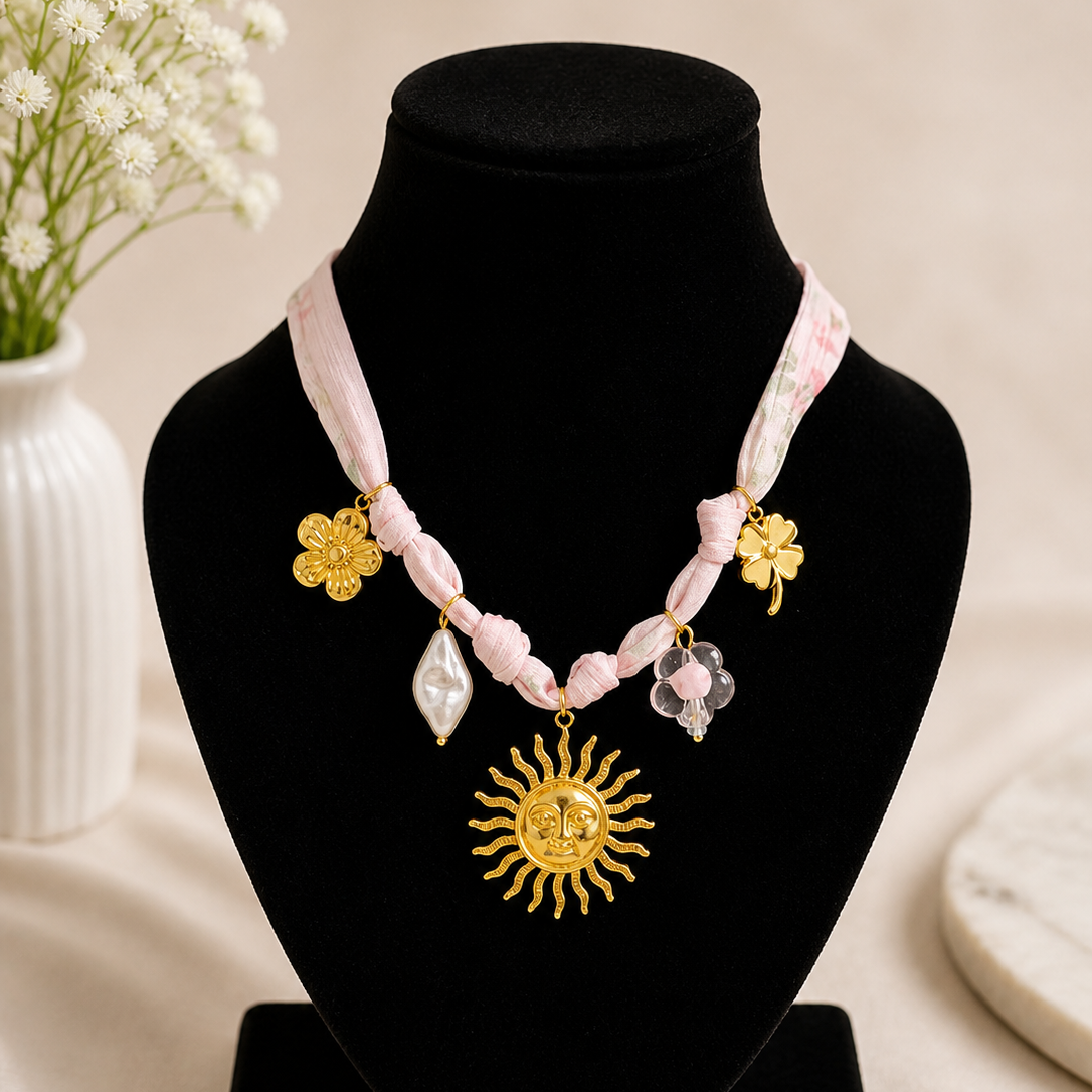 Necklace with pink beads and gold sun pendant on a black stand with white flowers in the background