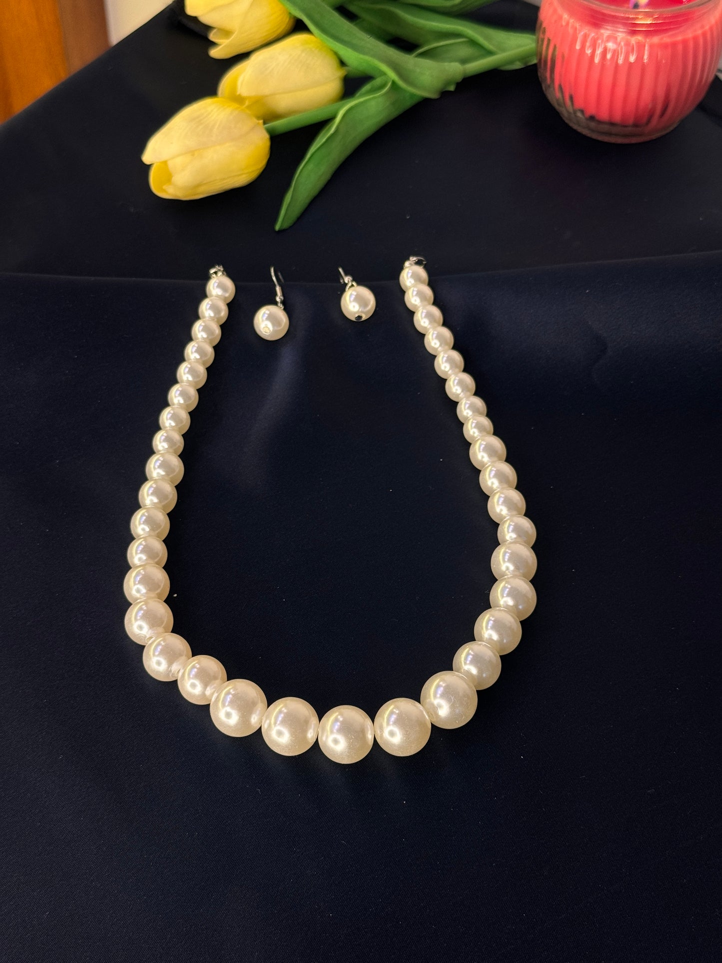 Pearl necklace and earrings on a dark surface with yellow tulips.
