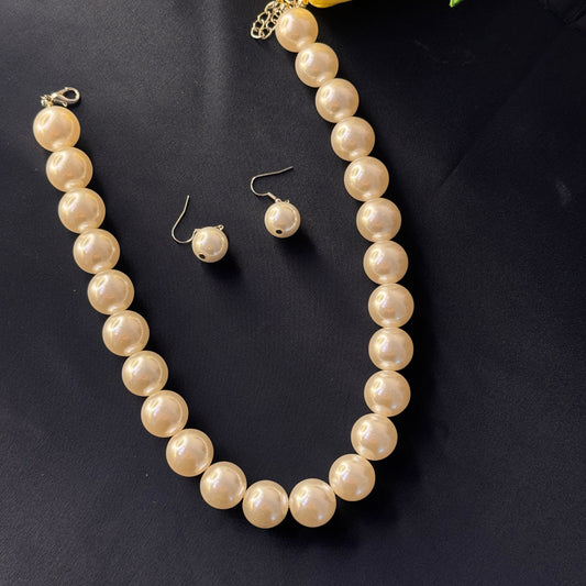 Pearl necklace and earrings on a dark fabric background with a yellow tulip.