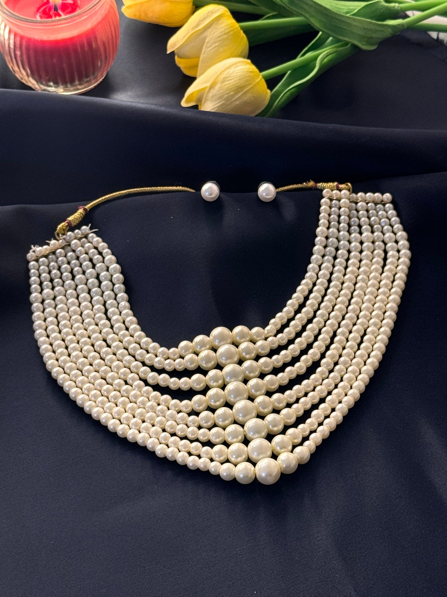 Pearl necklace on a dark fabric background with yellow tulips and a red object.