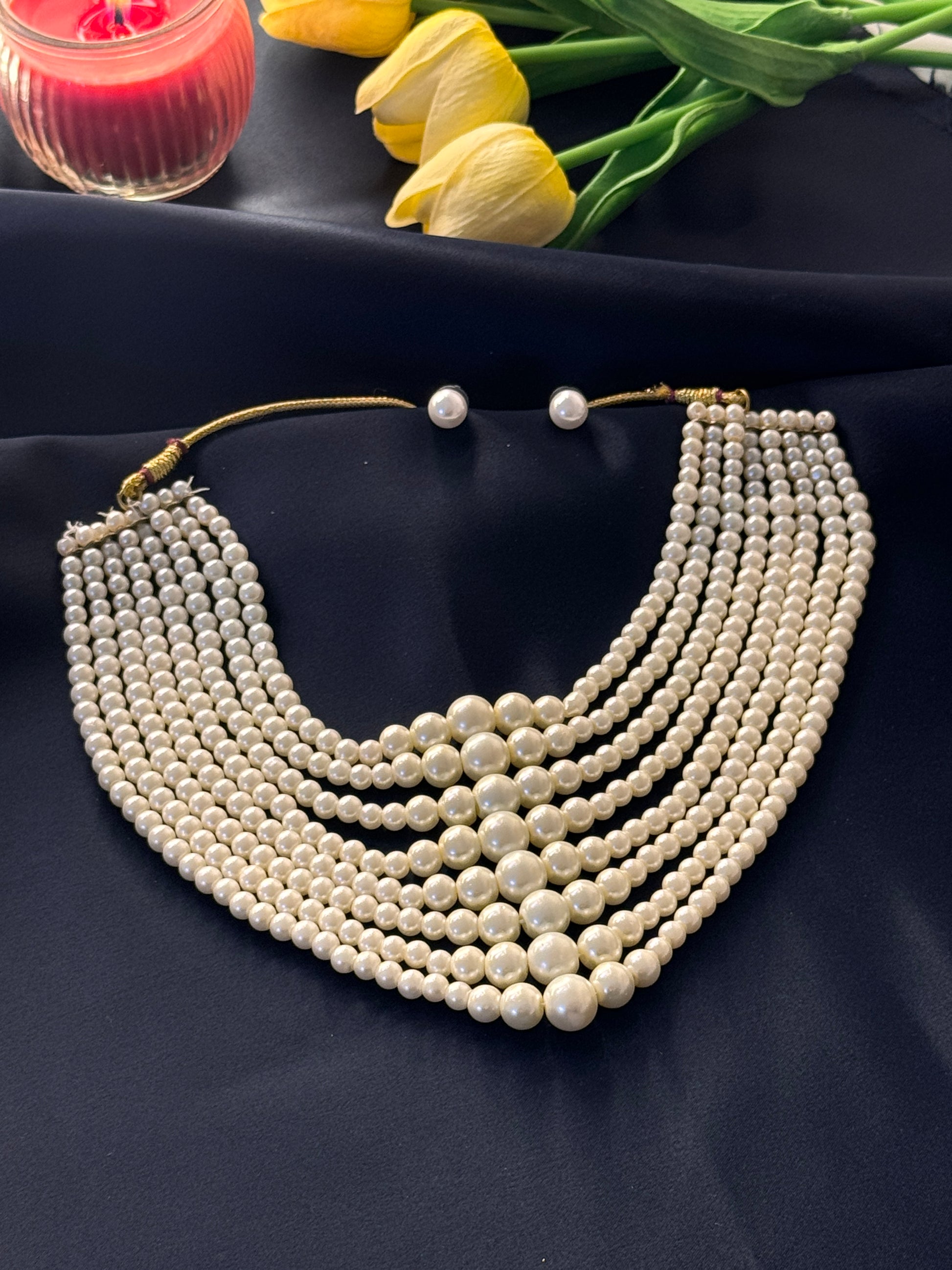 Pearl necklace on a dark fabric background with yellow tulips and a red object.