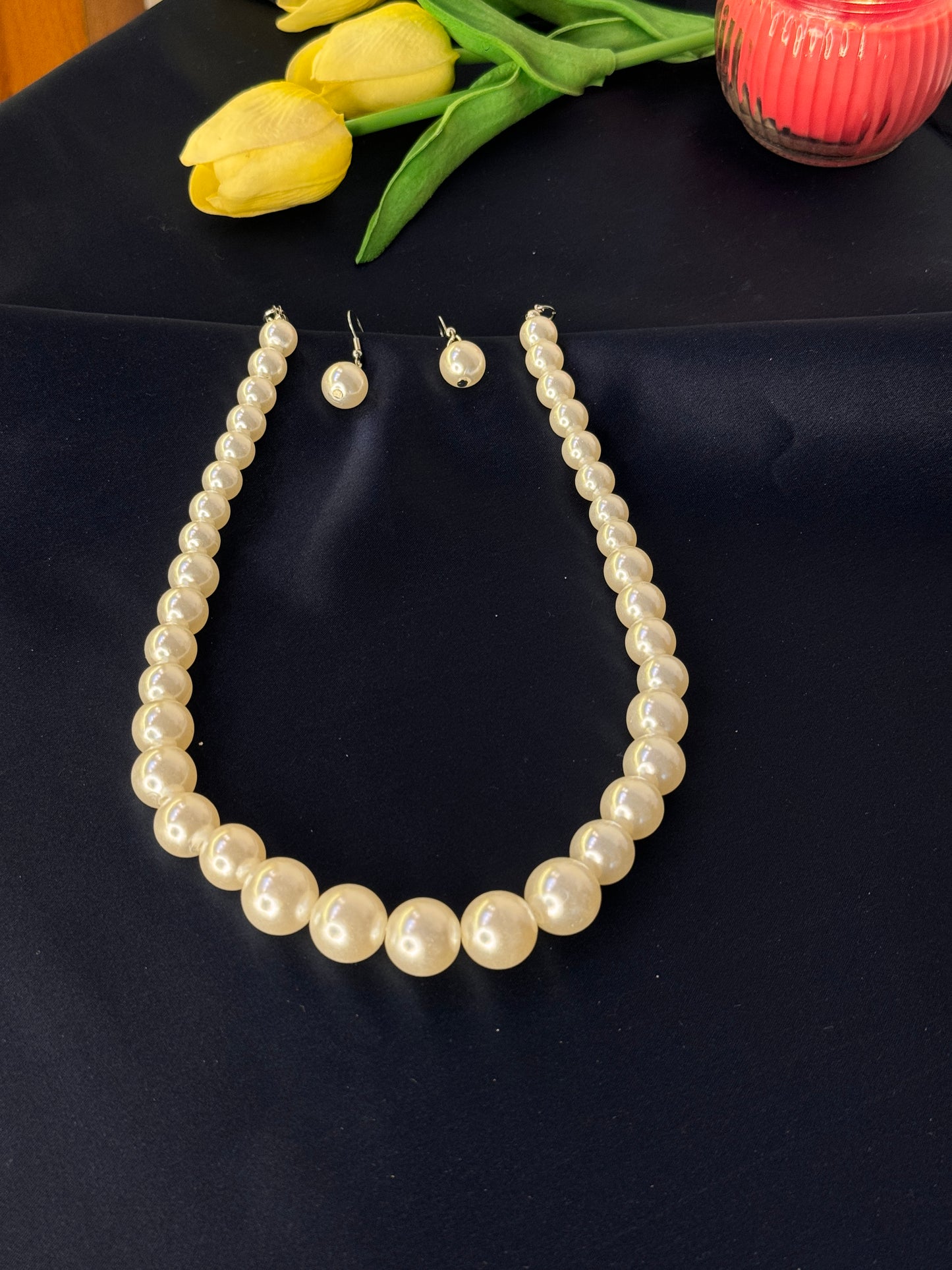 Pearl necklace and earrings on a dark fabric background with yellow tulips.