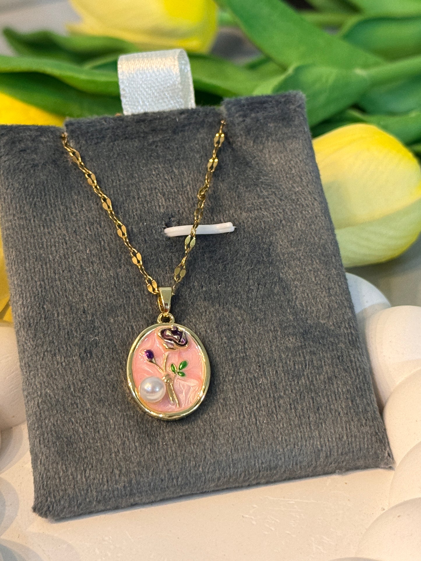 Necklace with a floral pendant on a gray jewelry pillow, surrounded by yellow tulips.