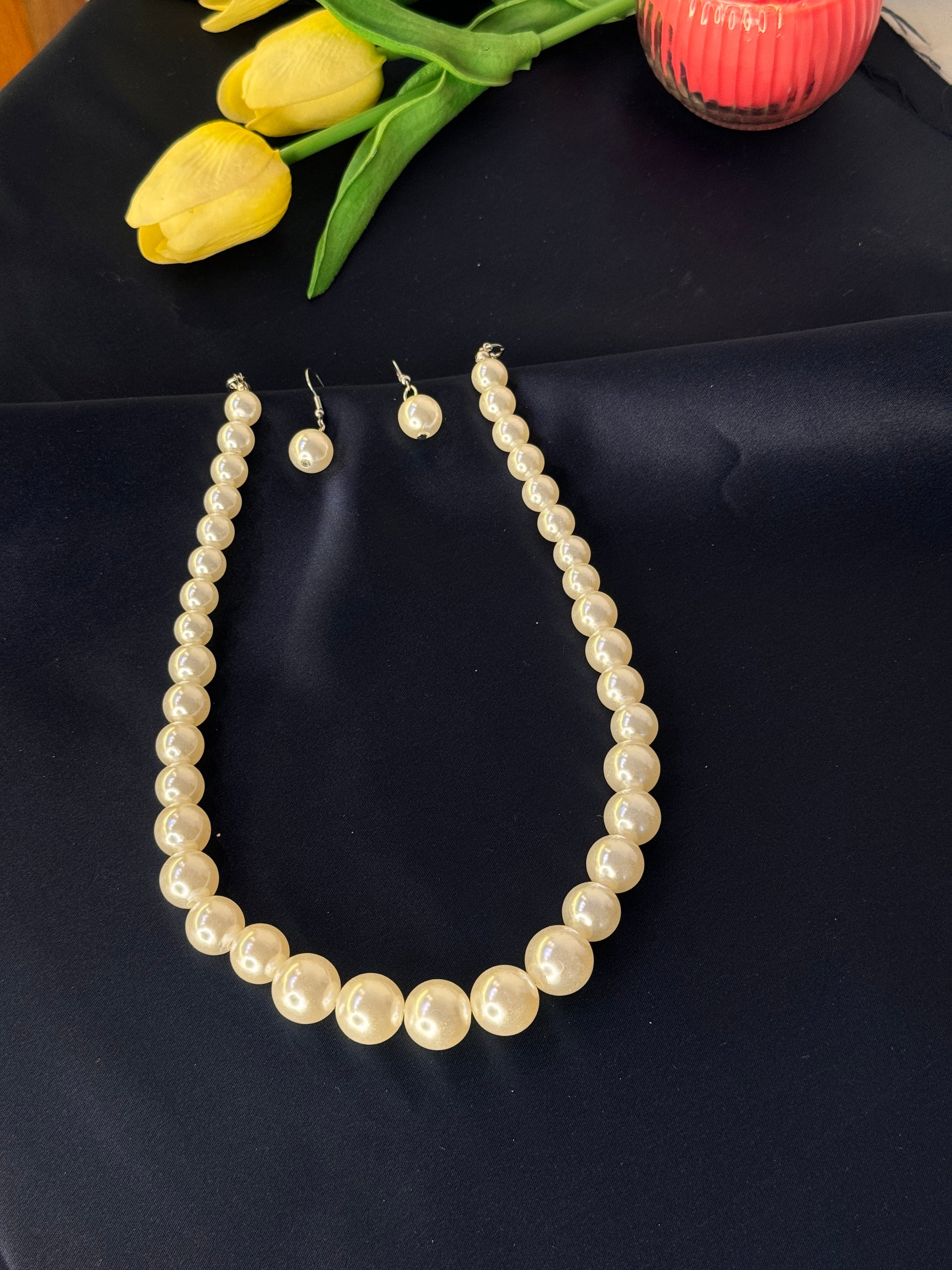 Pearl necklace and earrings on a dark surface with yellow tulips.
