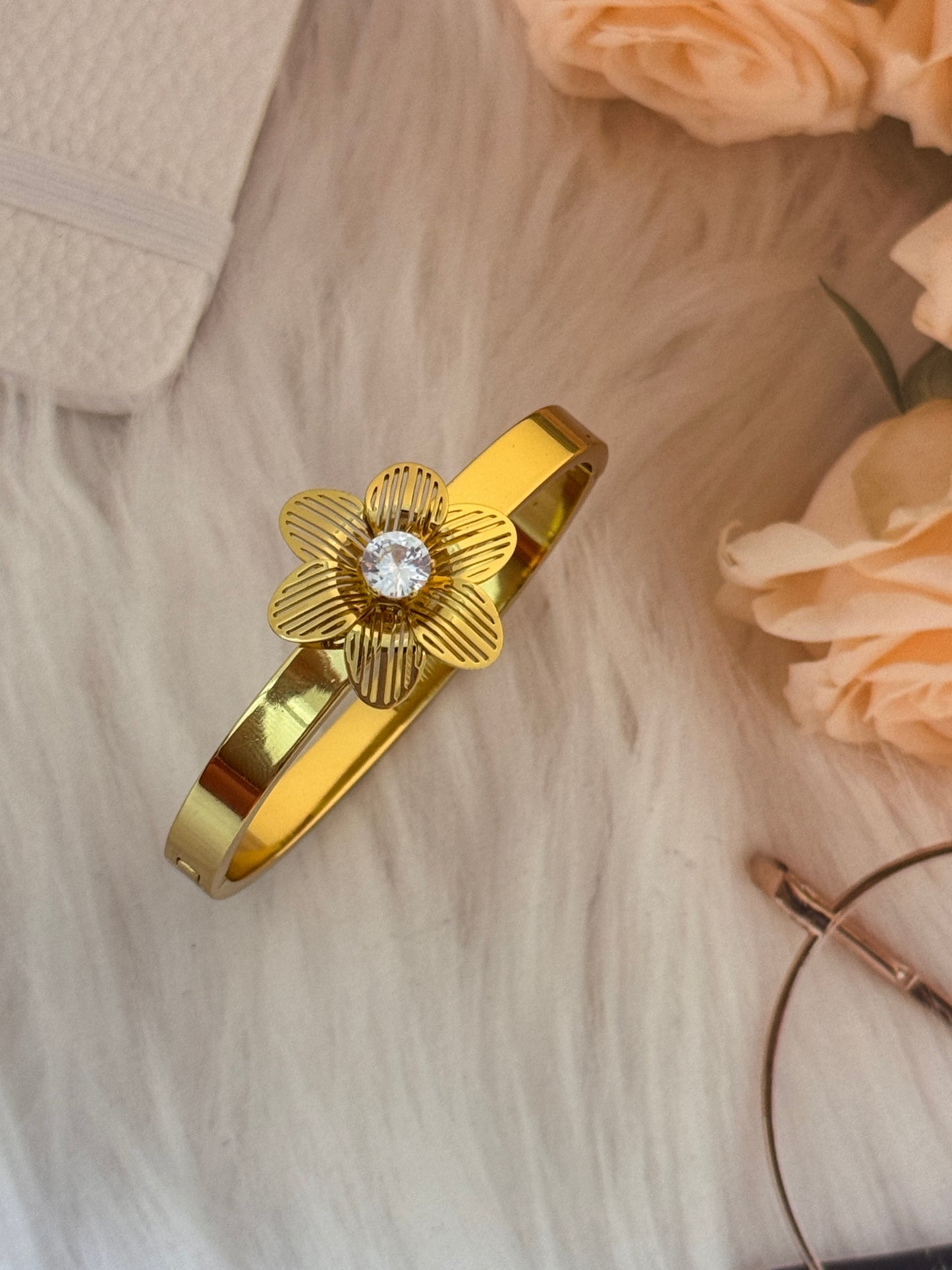 Gold bracelet with a floral design and diamond on a light wooden surface with flowers.