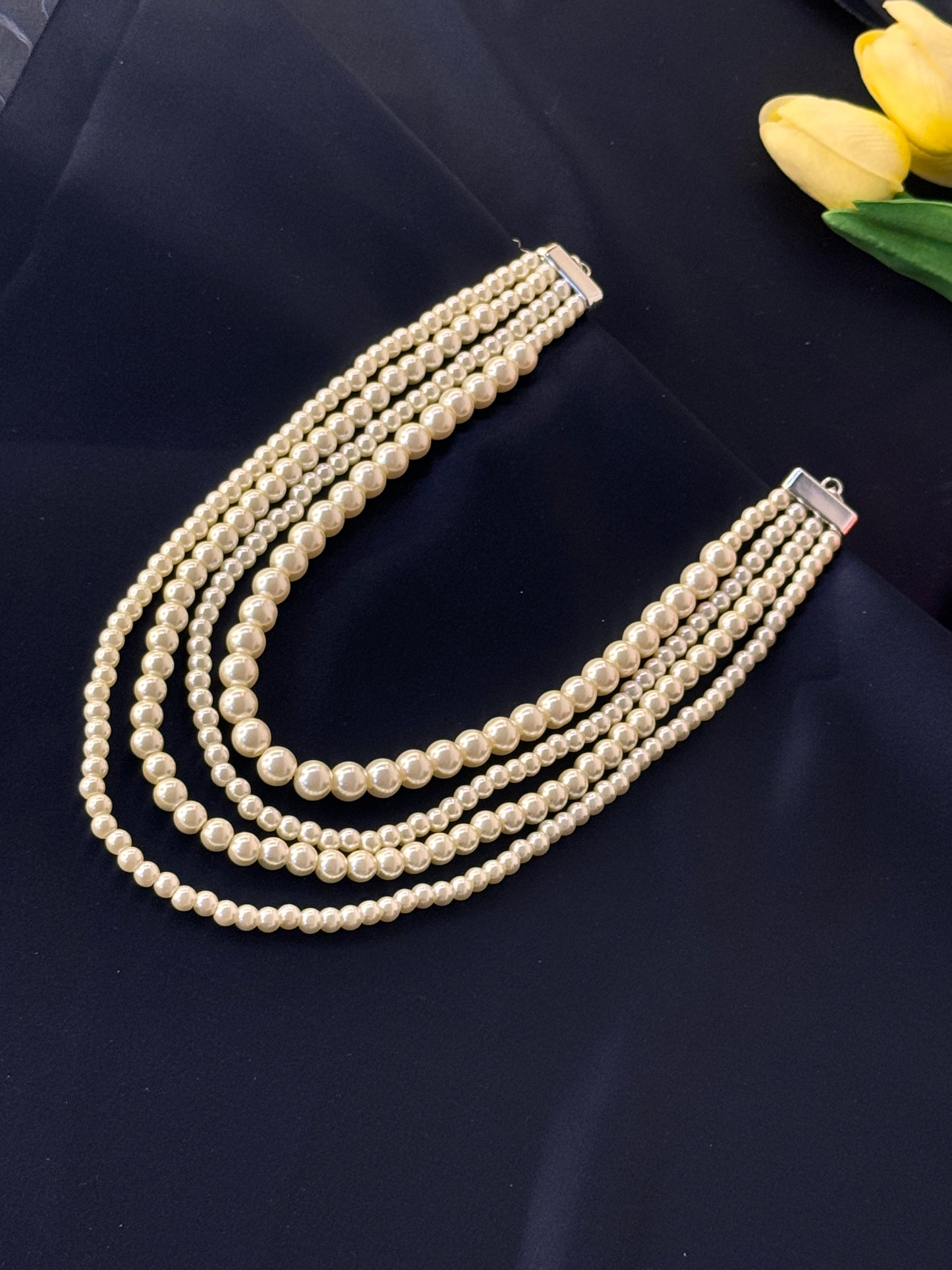 Pearl necklace on a dark surface with yellow tulips