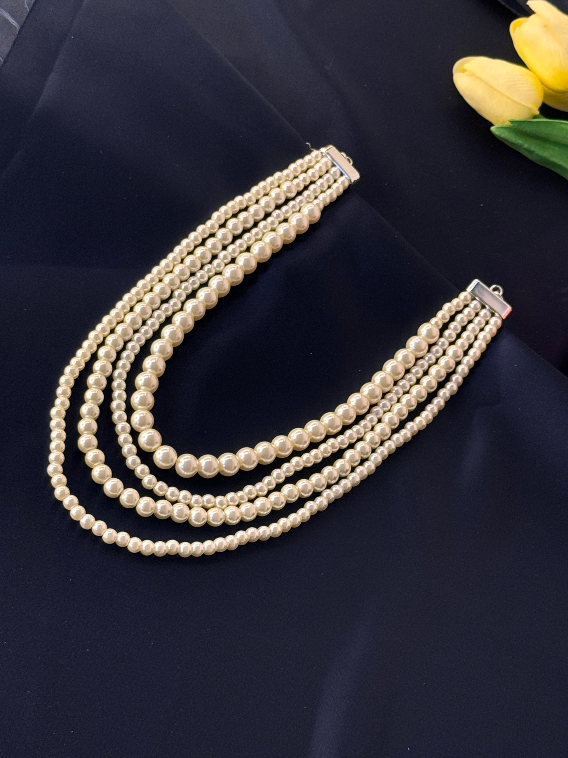 Pearl necklace on a dark surface with yellow tulips