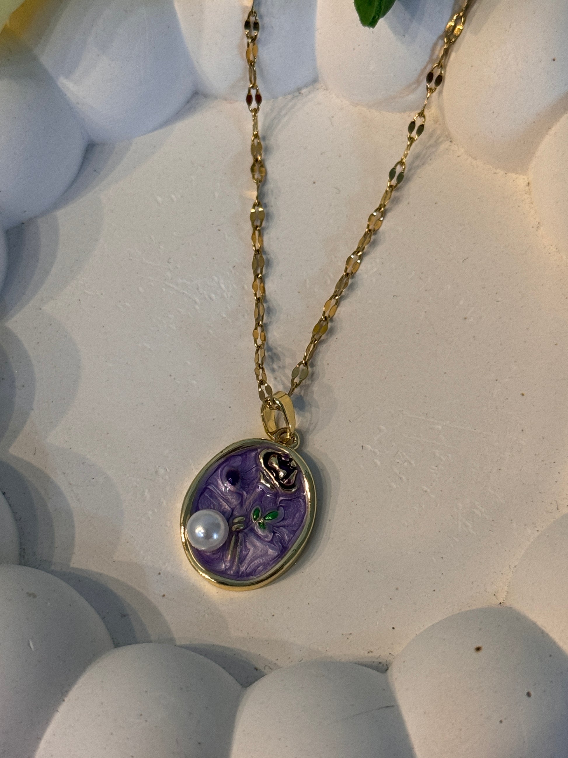 Necklace with a purple pendant and pearl on a textured white surface