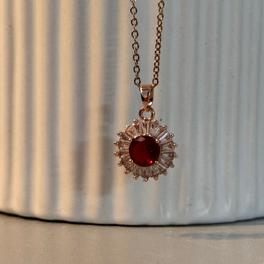 Necklace with a red gemstone and gold chain on a textured surface