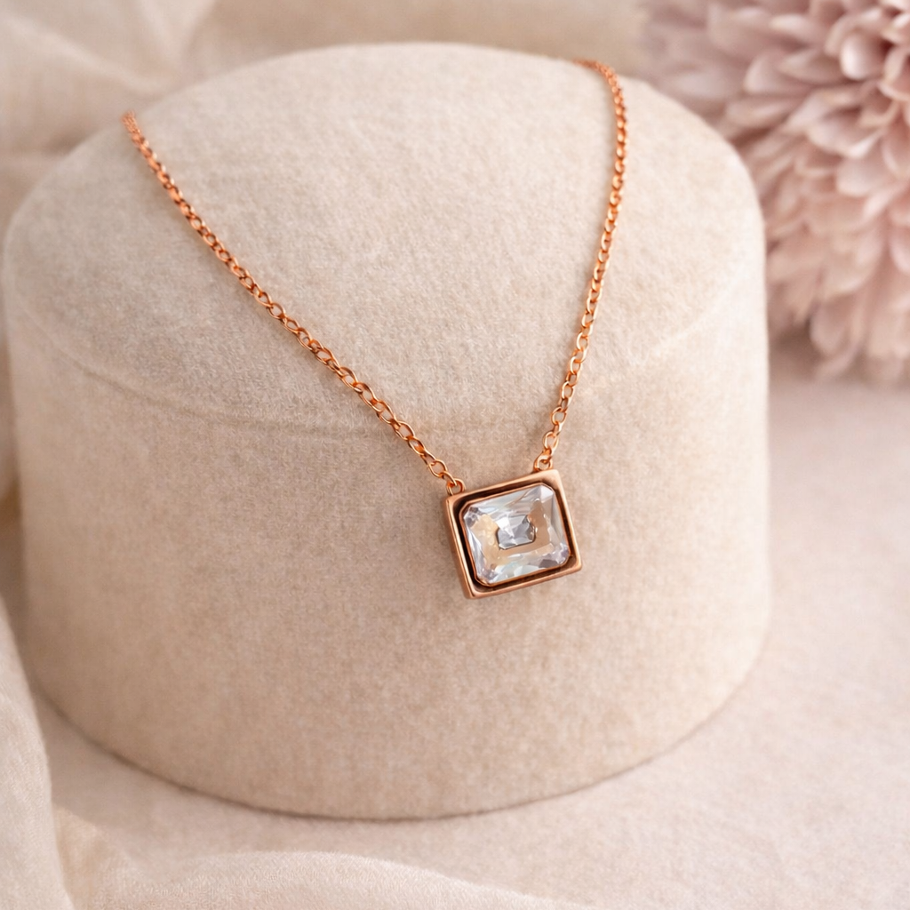 Rose gold necklace with a square pendant on a beige stand with a pink flower in the background