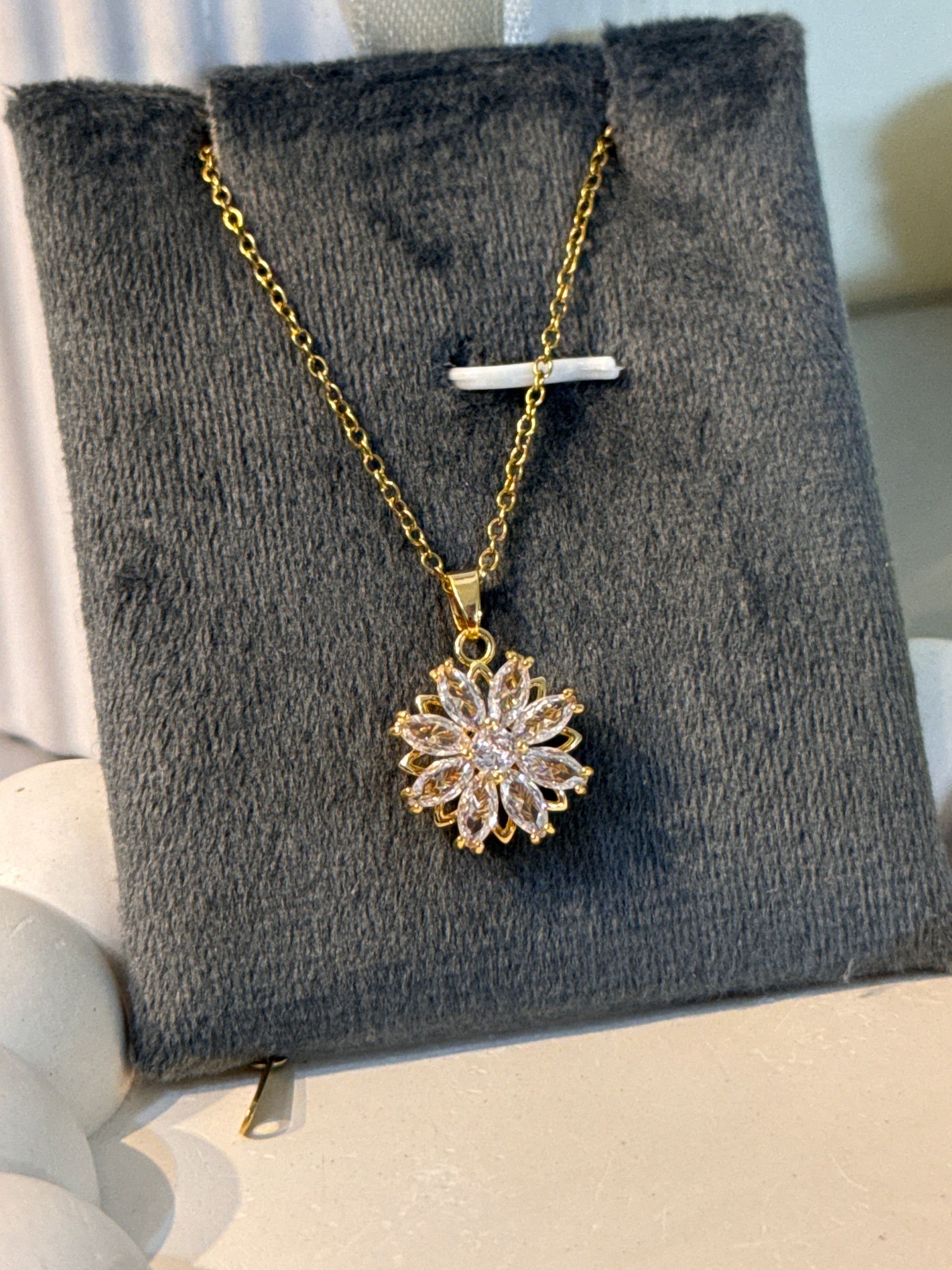 Gold necklace with a floral pendant on a gray jewelry display