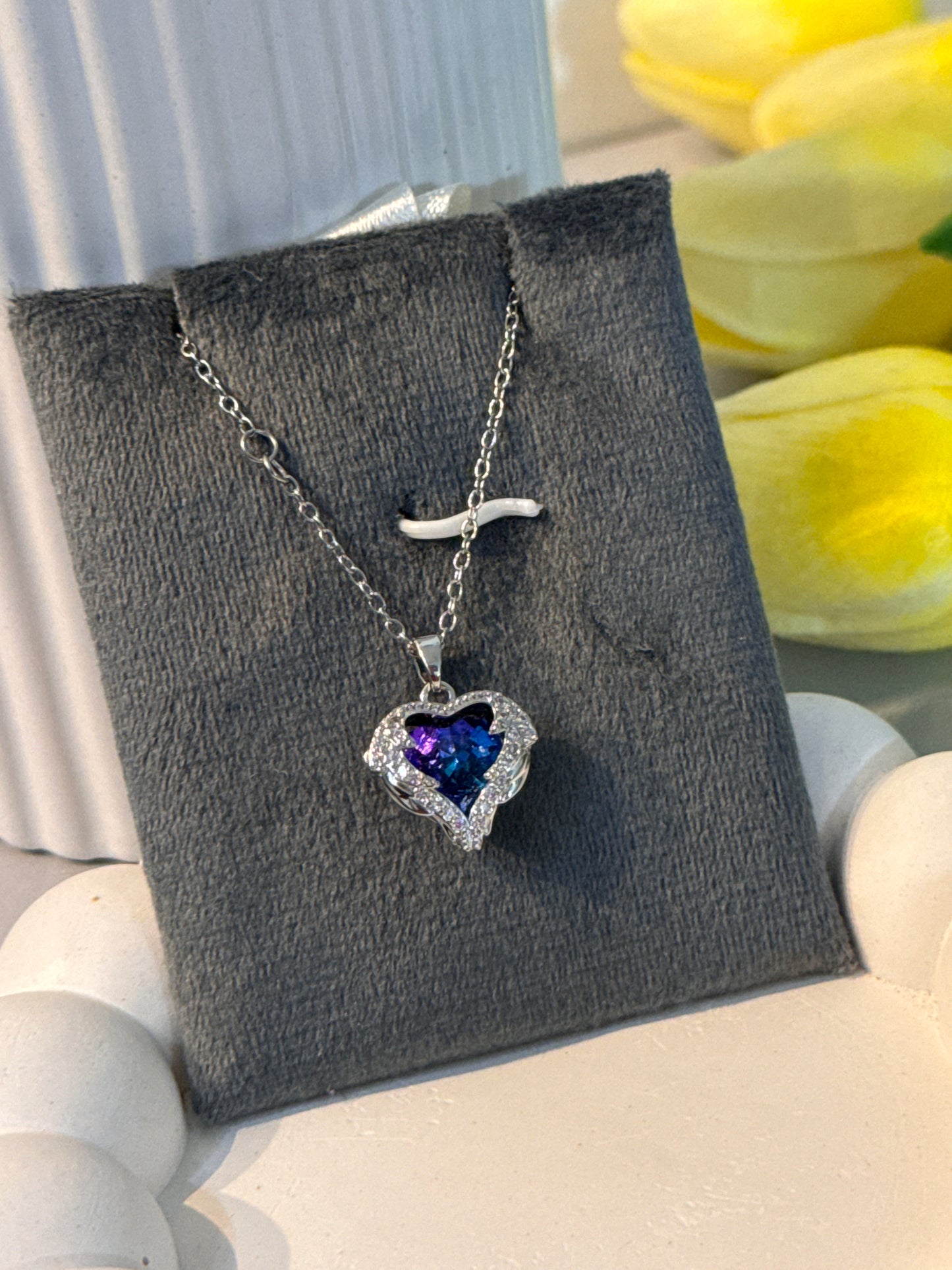 Necklace with a heart-shaped purple gemstone pendant on a gray card with flowers in the background