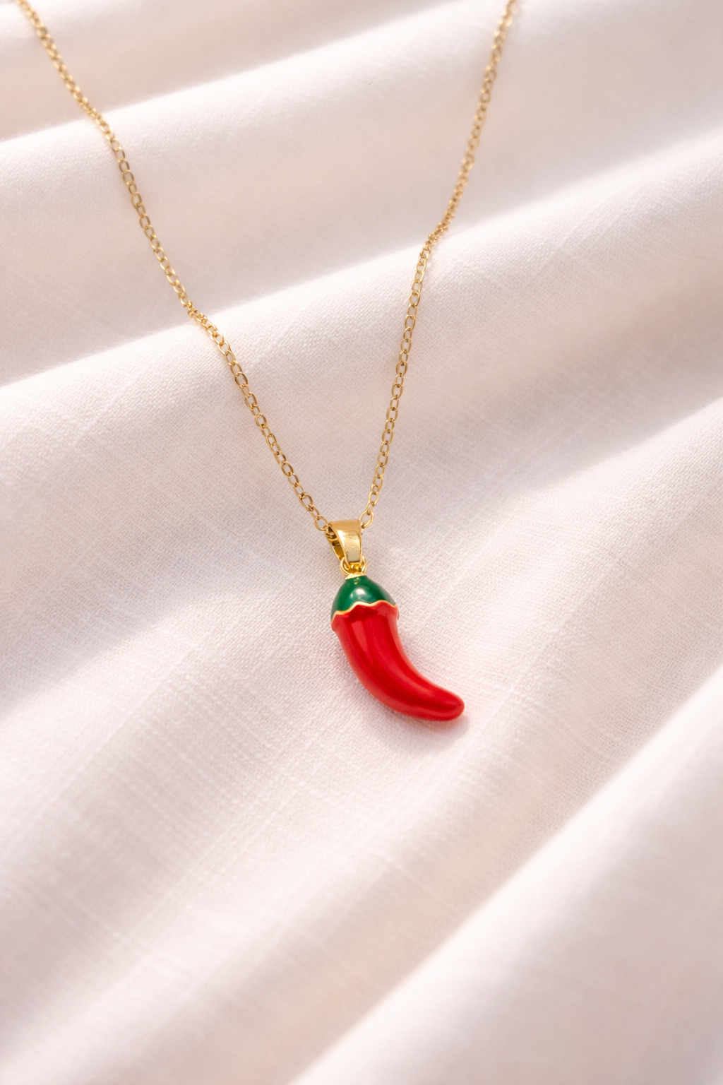 Red chili pepper pendant necklace on a gold chain against a beige fabric background