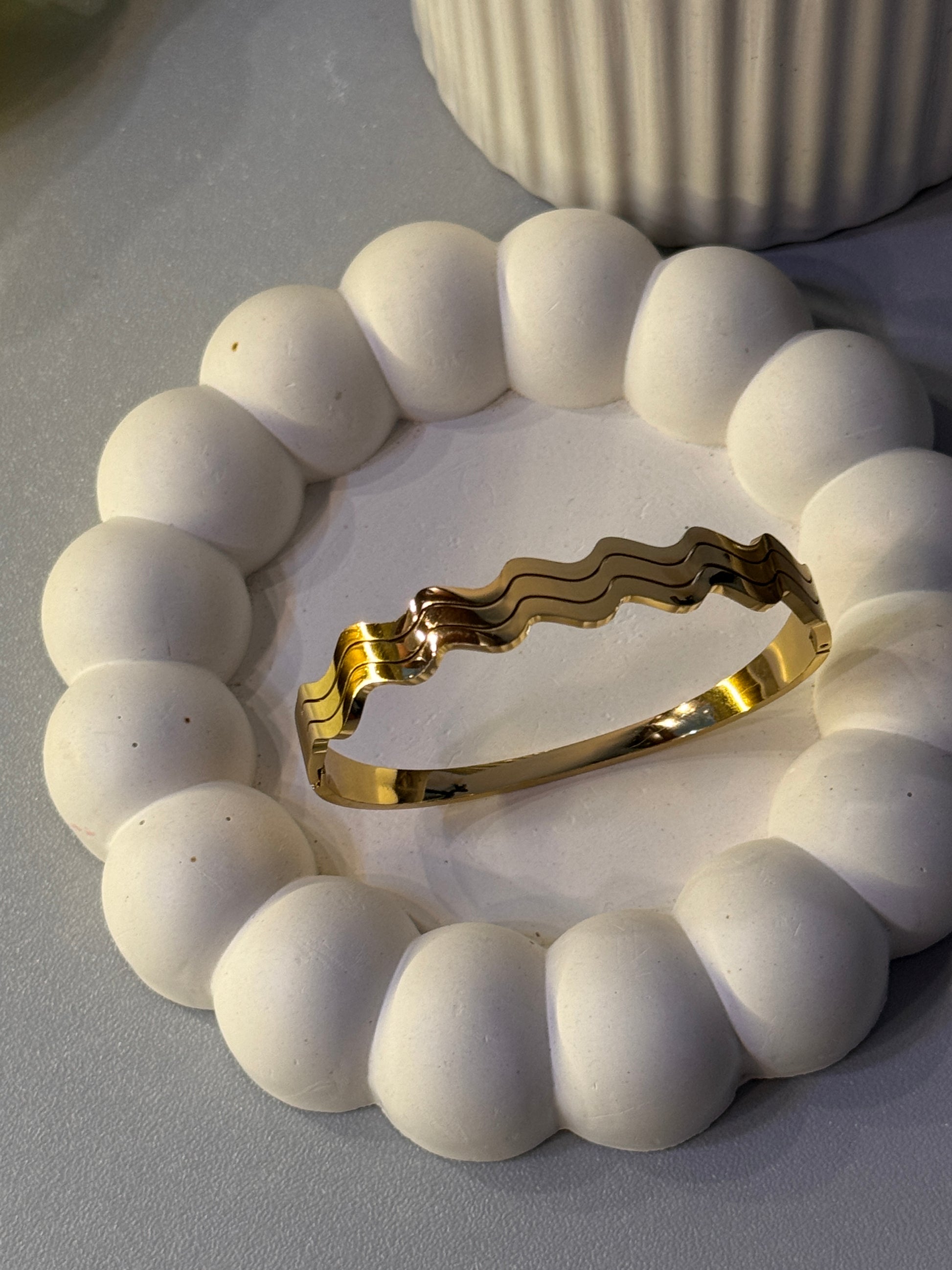 Gold bracelet on a white beaded bracelet against a neutral background