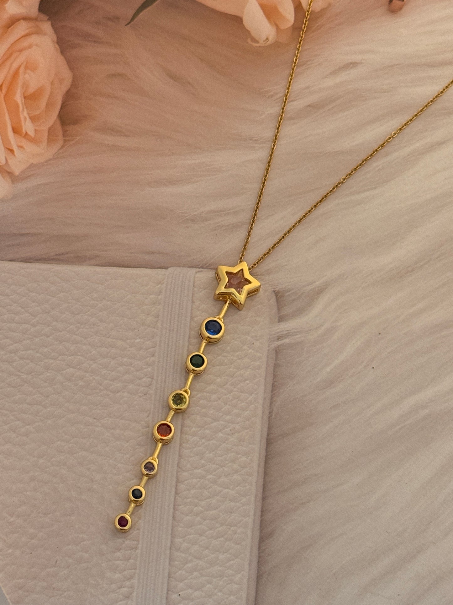 Gold necklace with star and colored stones on a textured beige surface