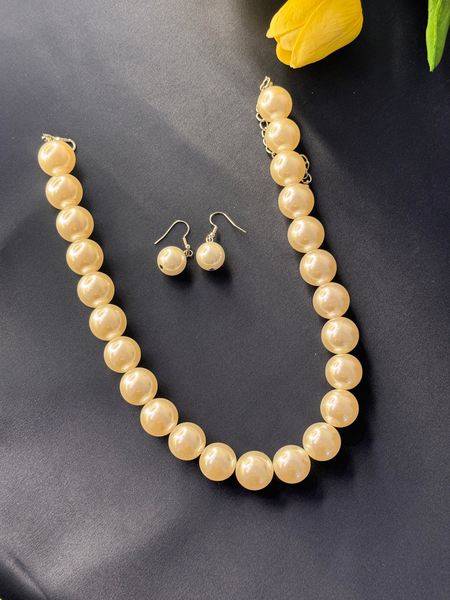 Pearl necklace and earrings on a dark surface with a yellow flower.