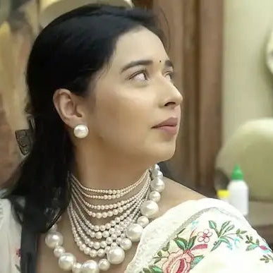 Woman wearing a traditional outfit with pearl jewelry indoors.