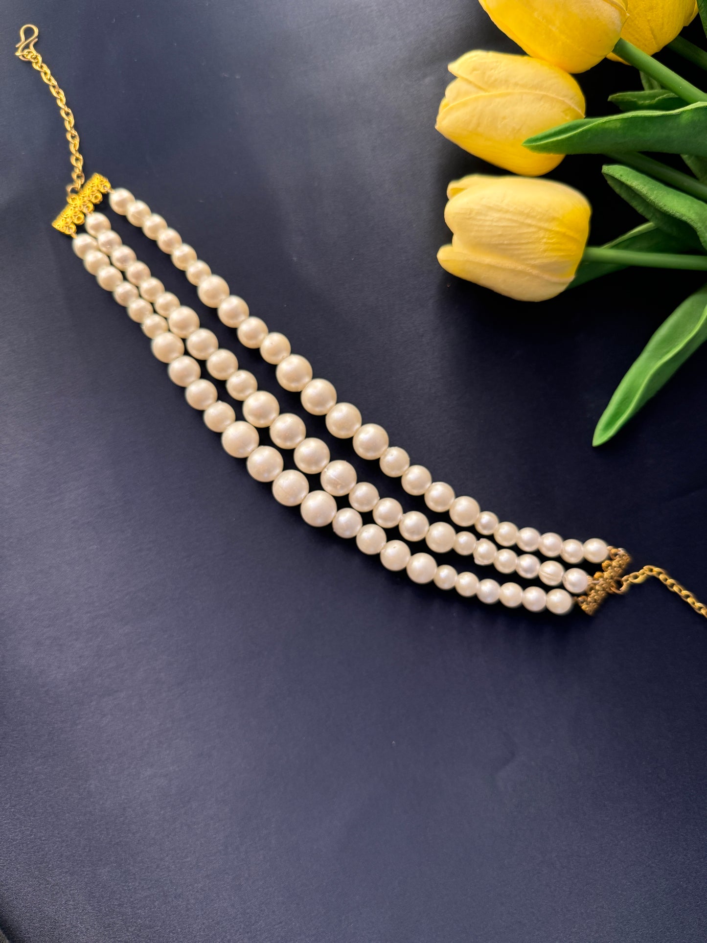 Pearl necklace with gold clasp on a dark surface with yellow tulips.