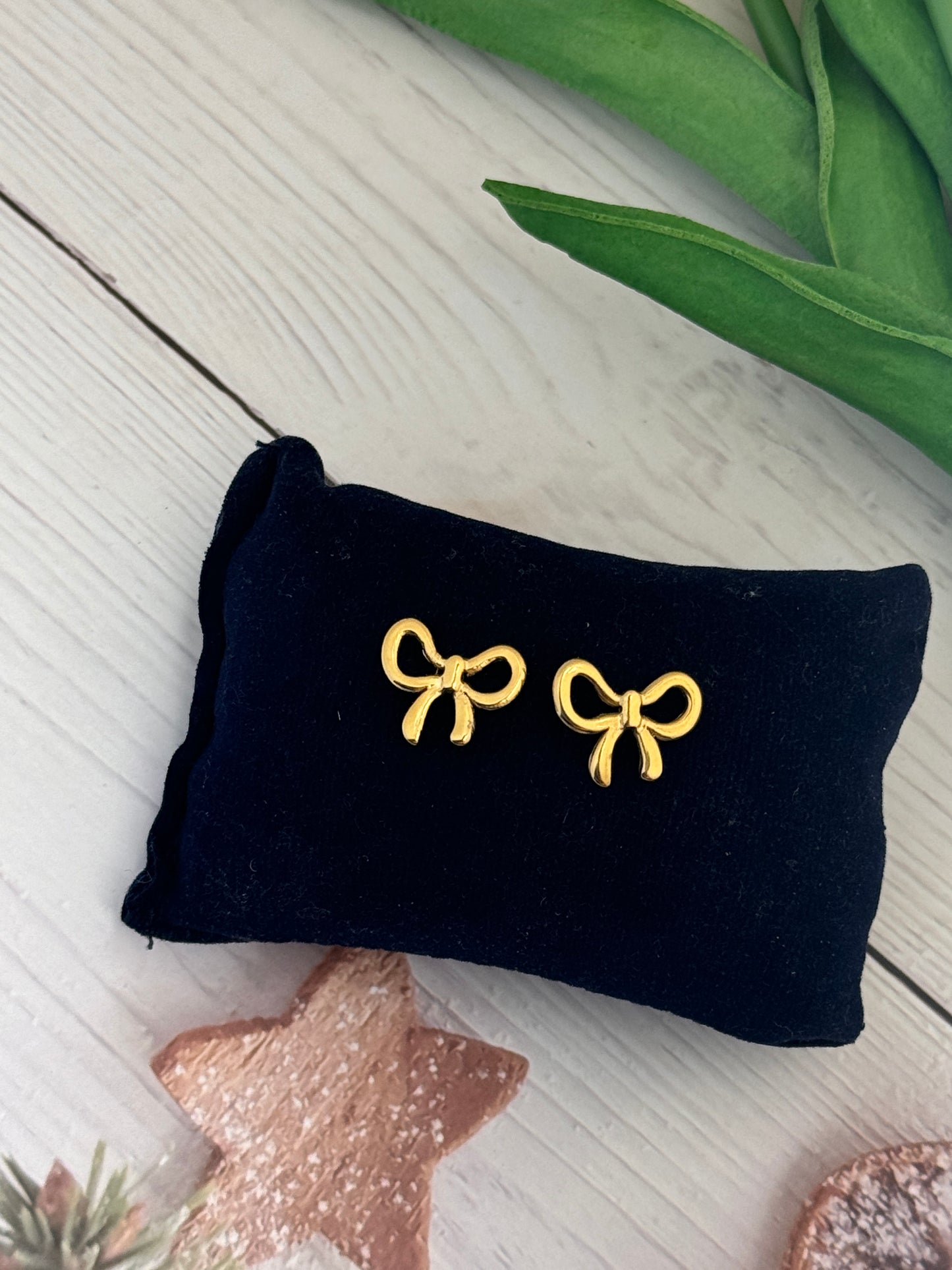 Black velvet jewelry pouch with gold bow-shaped earrings on a light wooden surface.