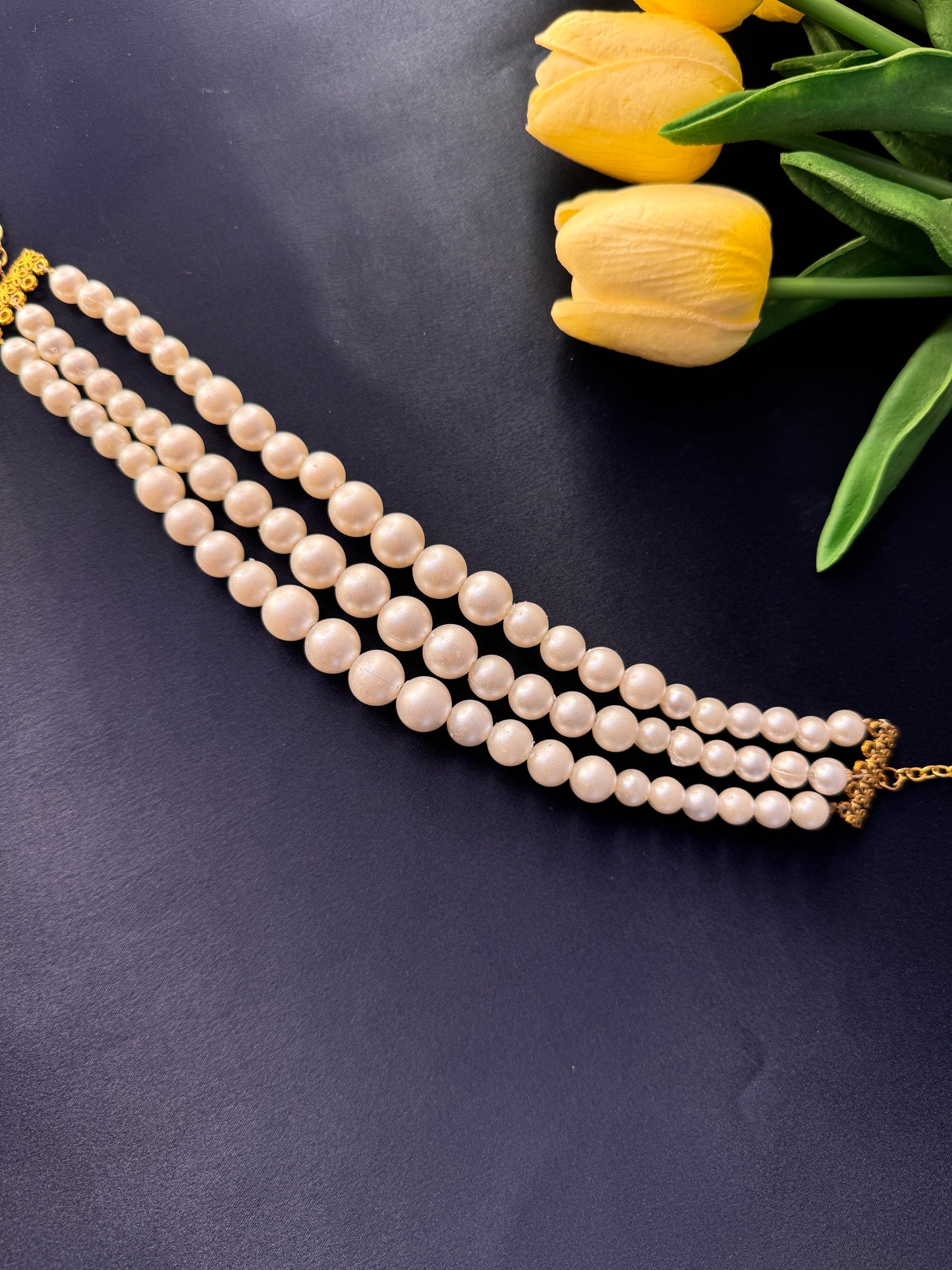 Pearl necklace with gold clasp on a dark background with yellow tulips