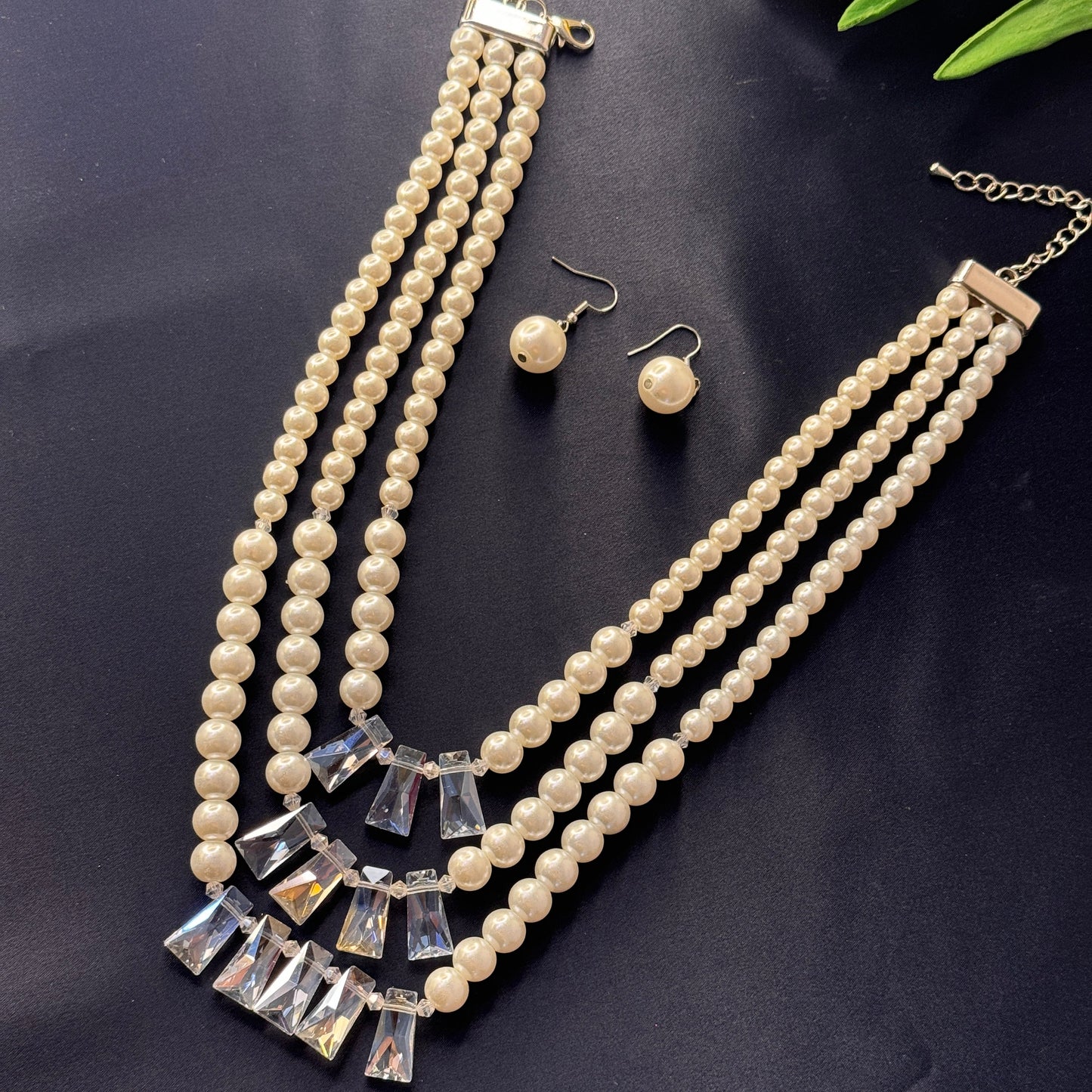 Pearl necklace with silver accents and matching earrings on a dark surface.