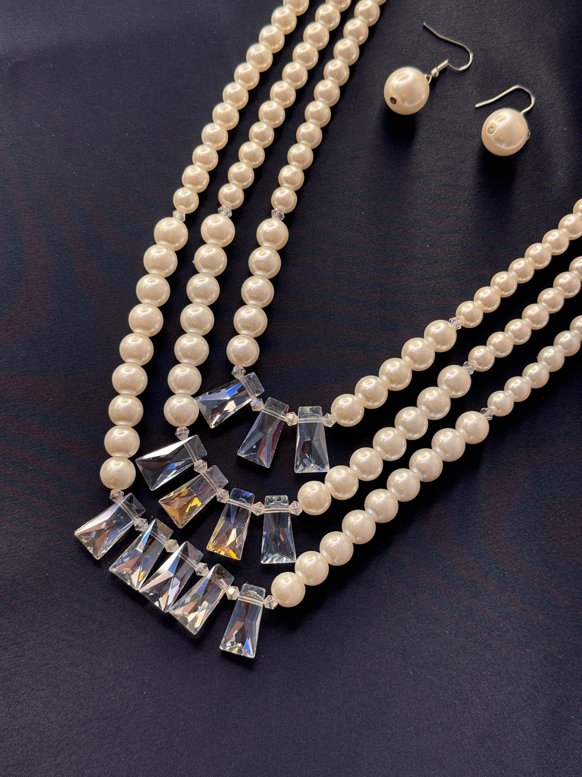 Pearl necklace with crystal pendants and matching earrings on a dark background