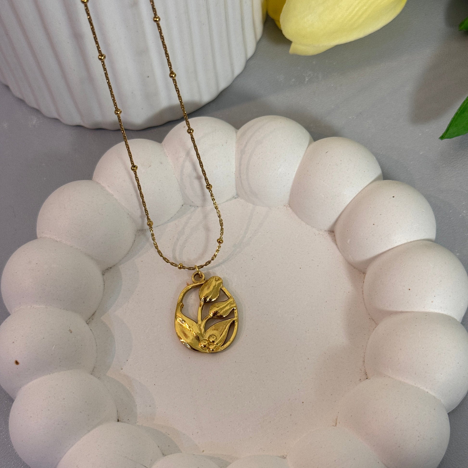 White beaded bracelet with a gold charm on a white surface with a yellow flower.